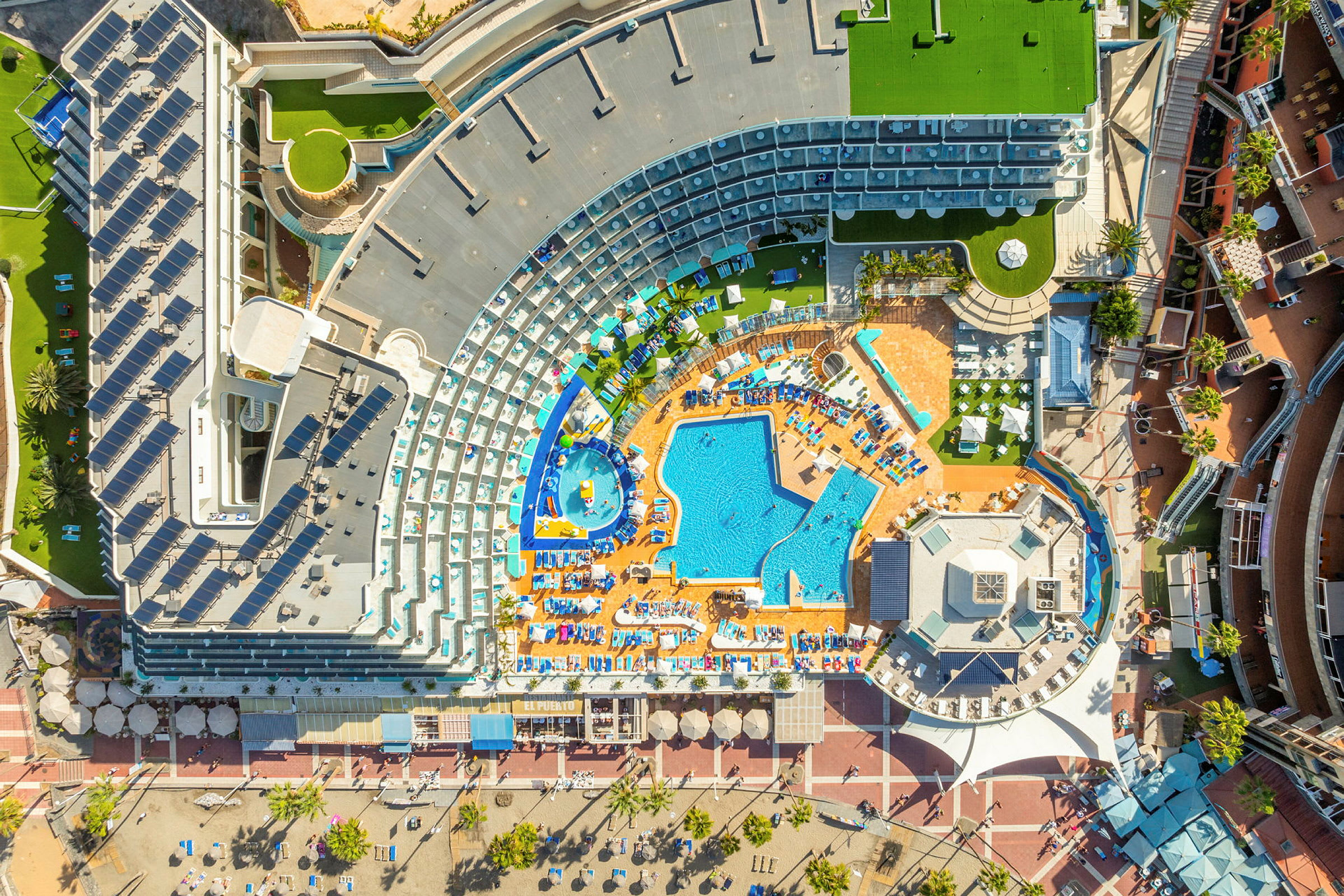 Flygbild av ett hotellkomplex med poolområden och omgivande byggnader. (AI-genererad text)