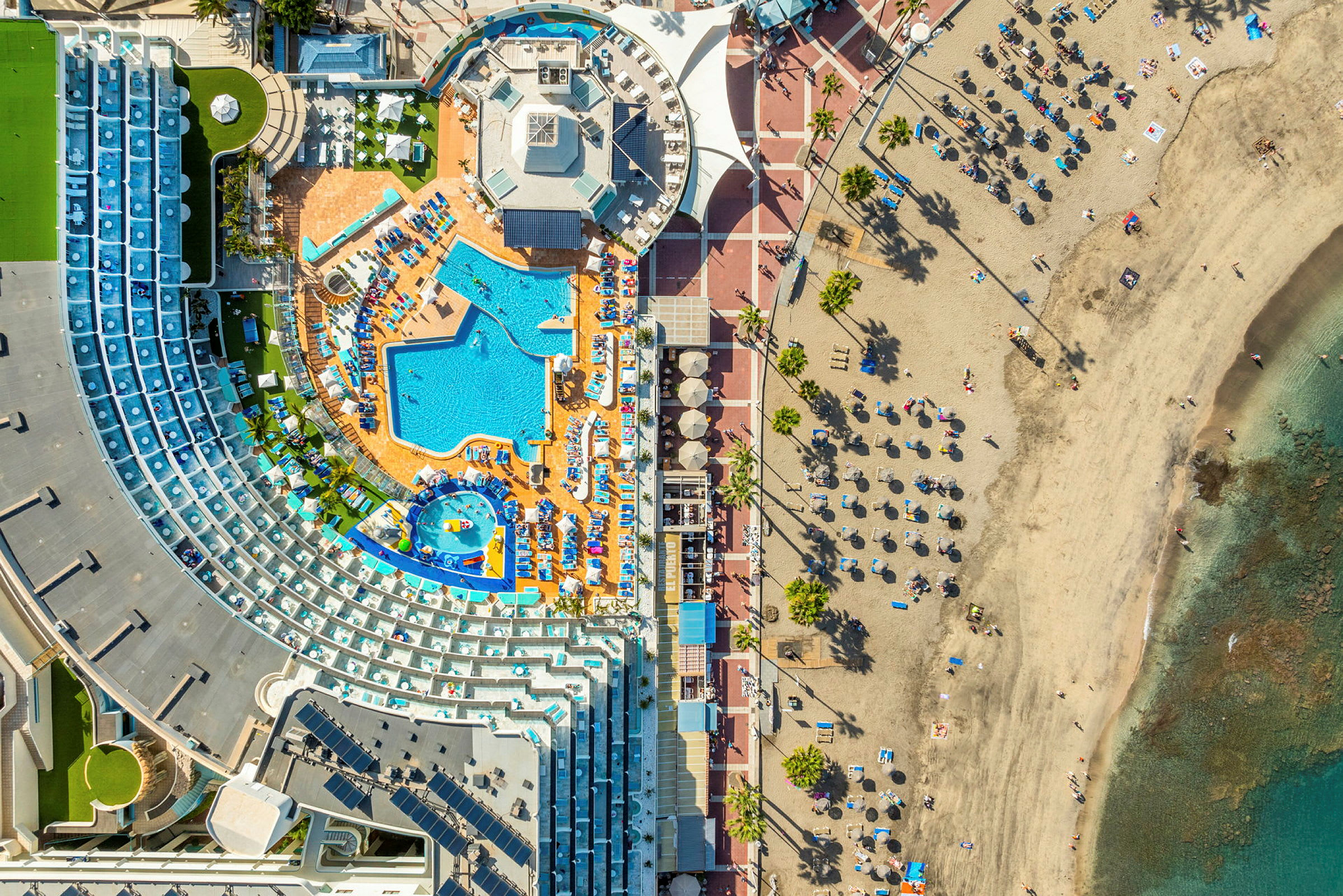 Flygbild över hotellområde med pool och strand. (AI-genererad text)