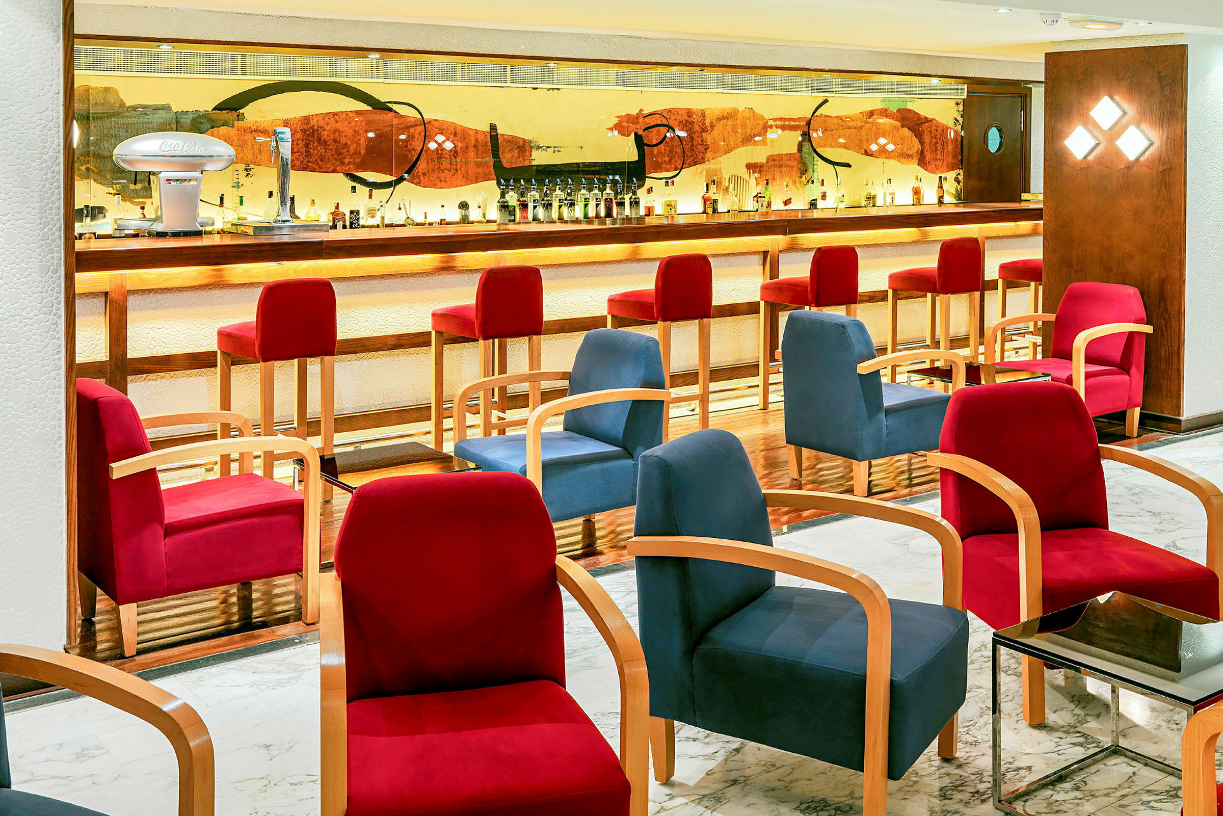 En hotellbar med upplyst bardisk, höga röda stolar, och bekväma sittmöbler i olika färger. (AI-genererad text)