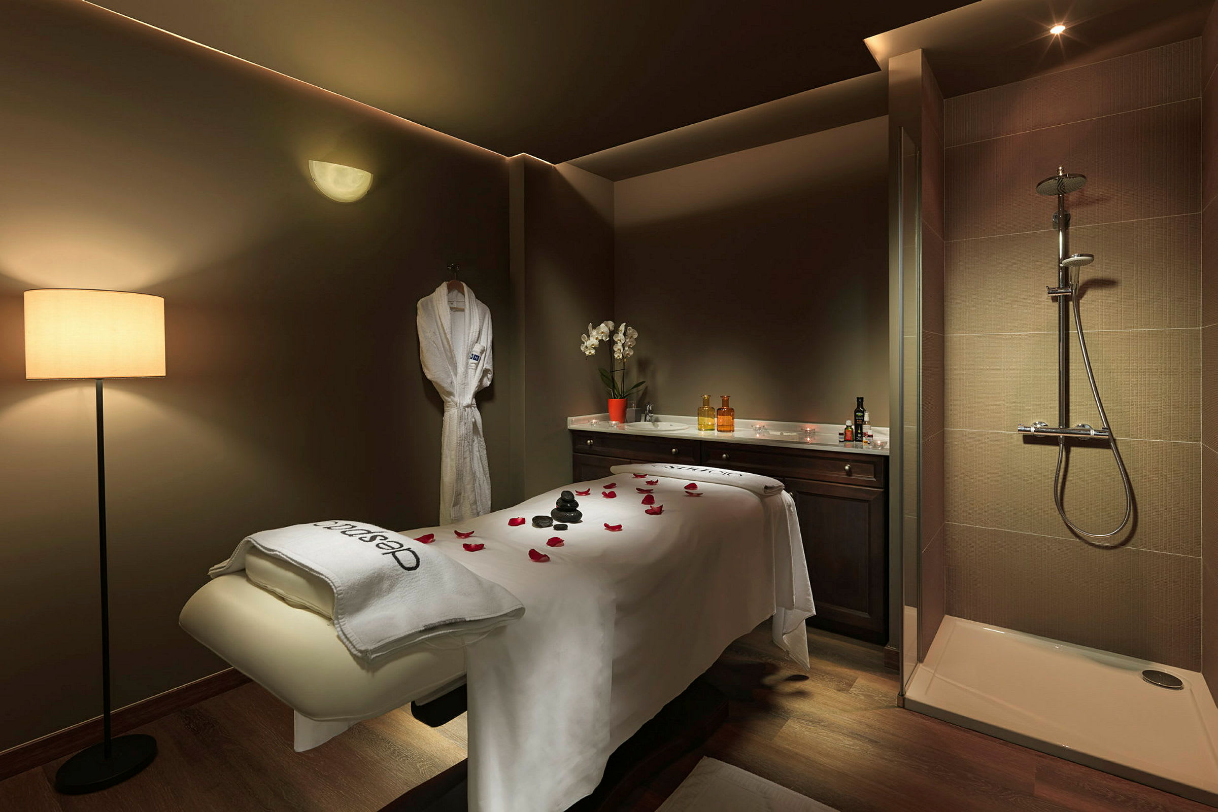Ett rum för spa- eller massagebehandling med en behandlingsbänk, en dusch, och en badrock hängande på väggen. (AI-genererad text)