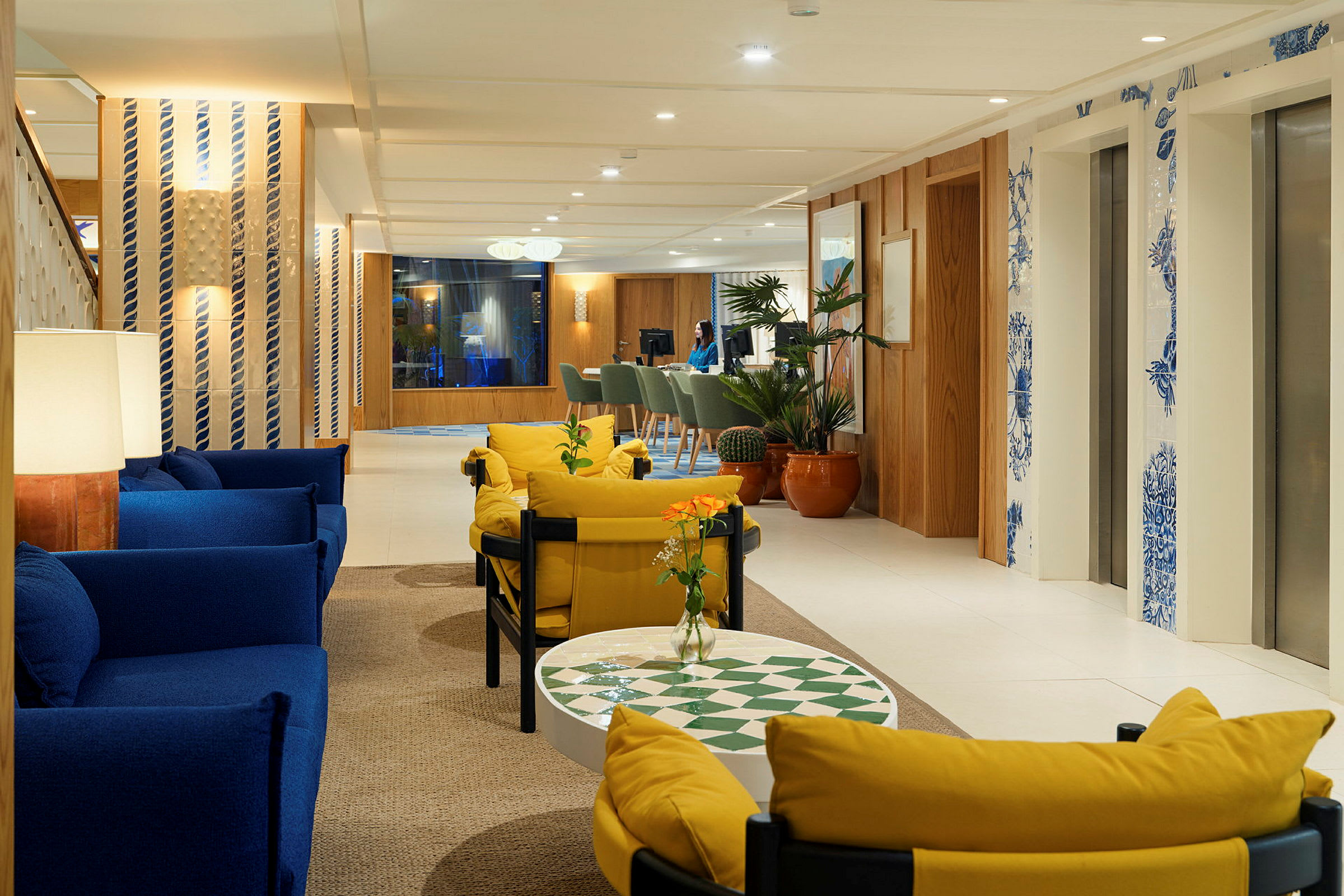 En ljus hotellobby med soffor i blått och gult, växter och hissar dekorerade med blå detaljer. (AI-genererad text)