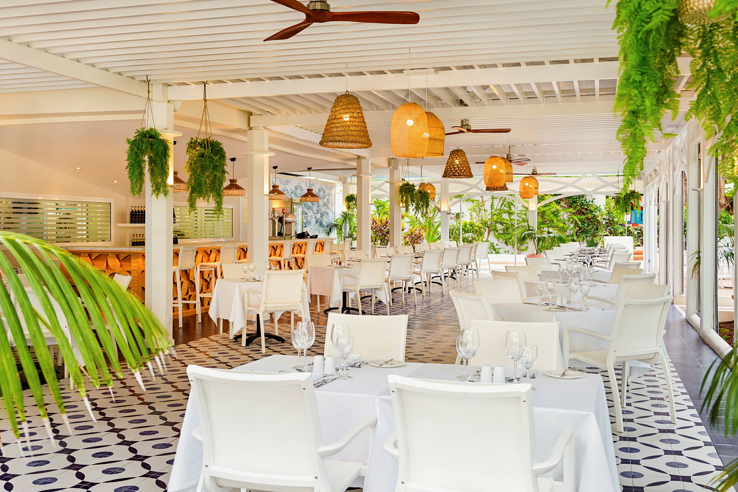 Ett luftigt restaurangområde med vita möbler, grön växtdekoration och taklampor av rotting. (AI-genererad text)