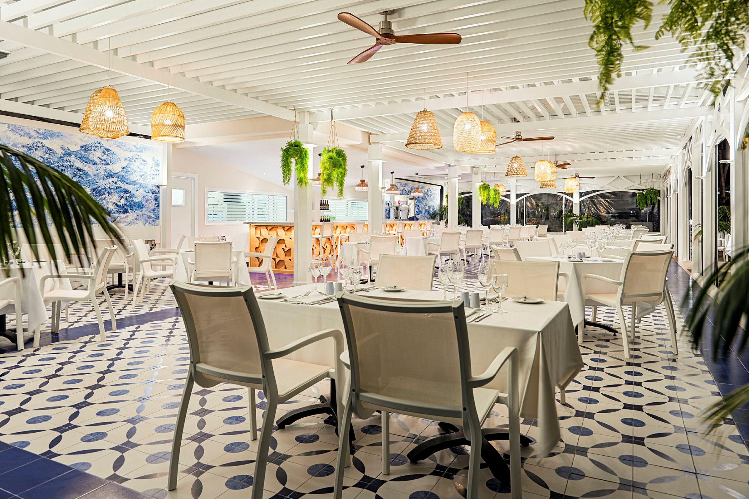 En ljus restaurang med vita bordsdukar och moderna möbler. Taklampor och växter hänger från taket. (AI-genererad text)