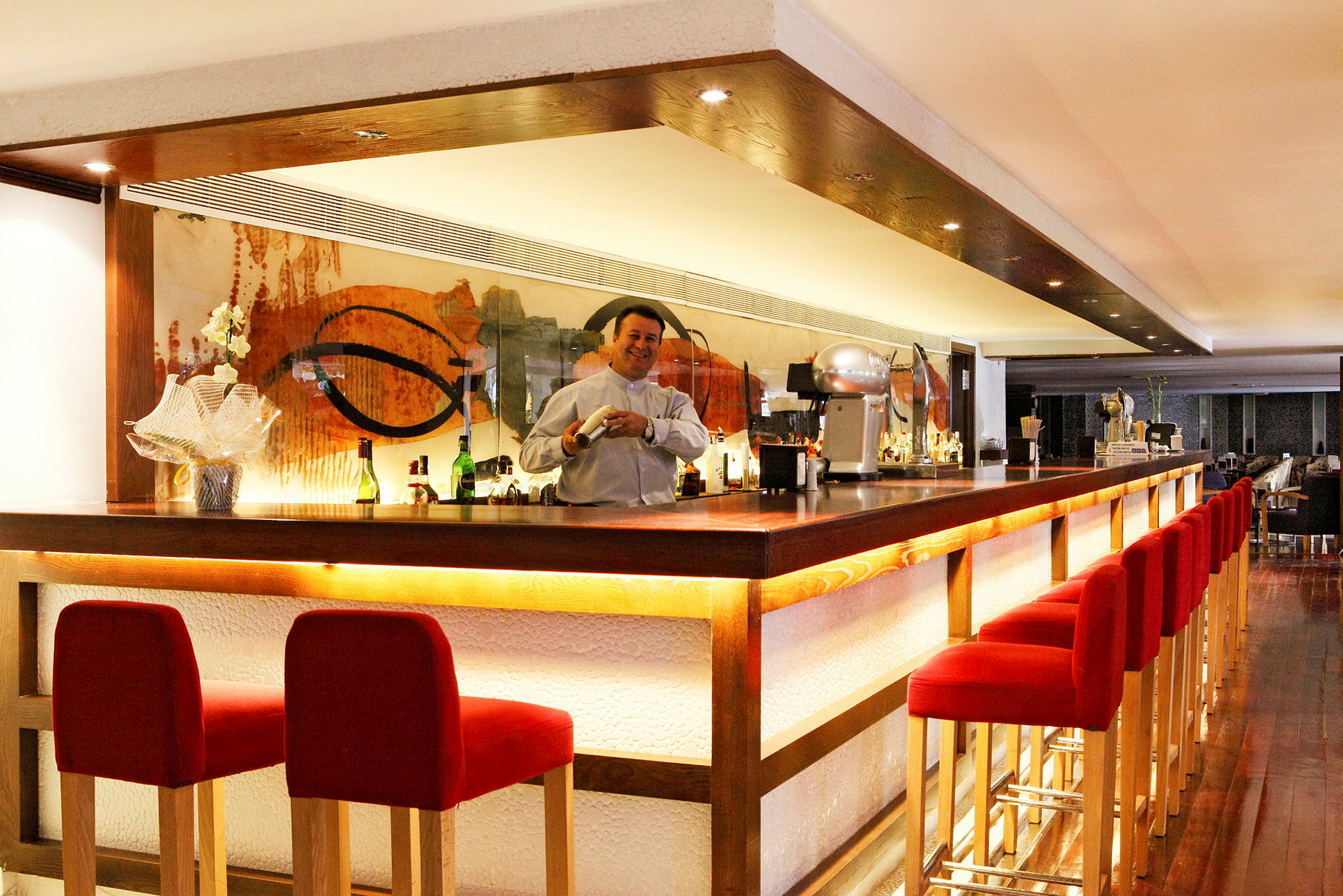 En bar med röda barstolar och en bartender som står bakom bardisken. (AI-genererad text)