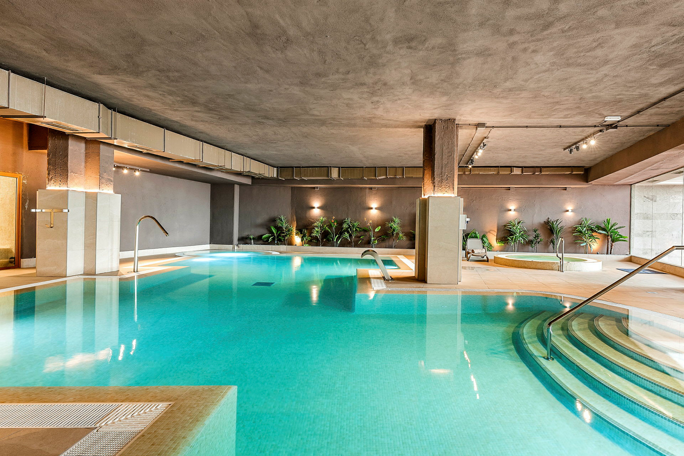 Interiör av ett spaområde med en inomhuspool, jacuzzi och växter som dekoration. (AI-genererad text)