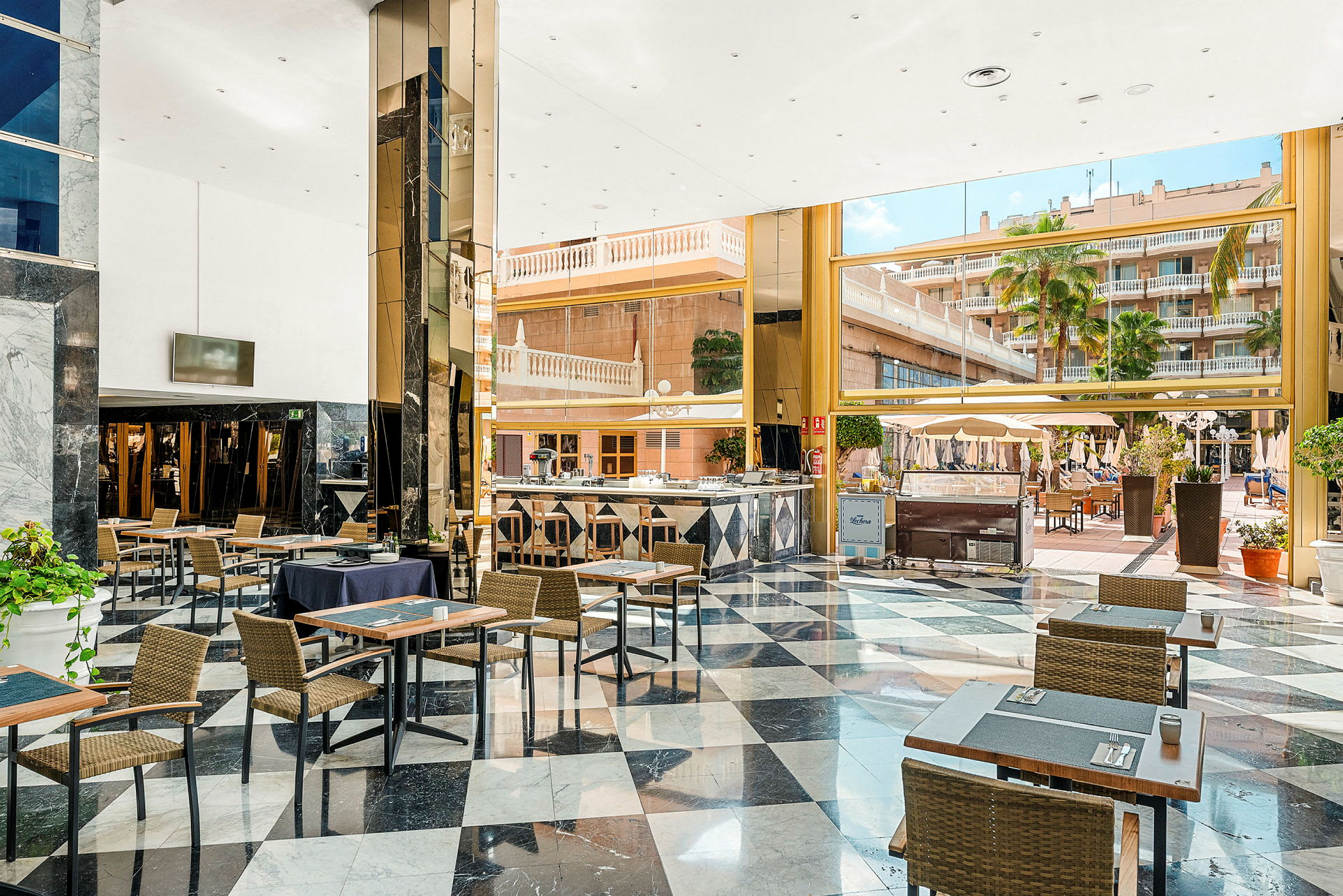 En rymlig hotellobby med bord och stolar, stora fönster med utsikt över en uteplats och poolområde. (AI-genererad text)