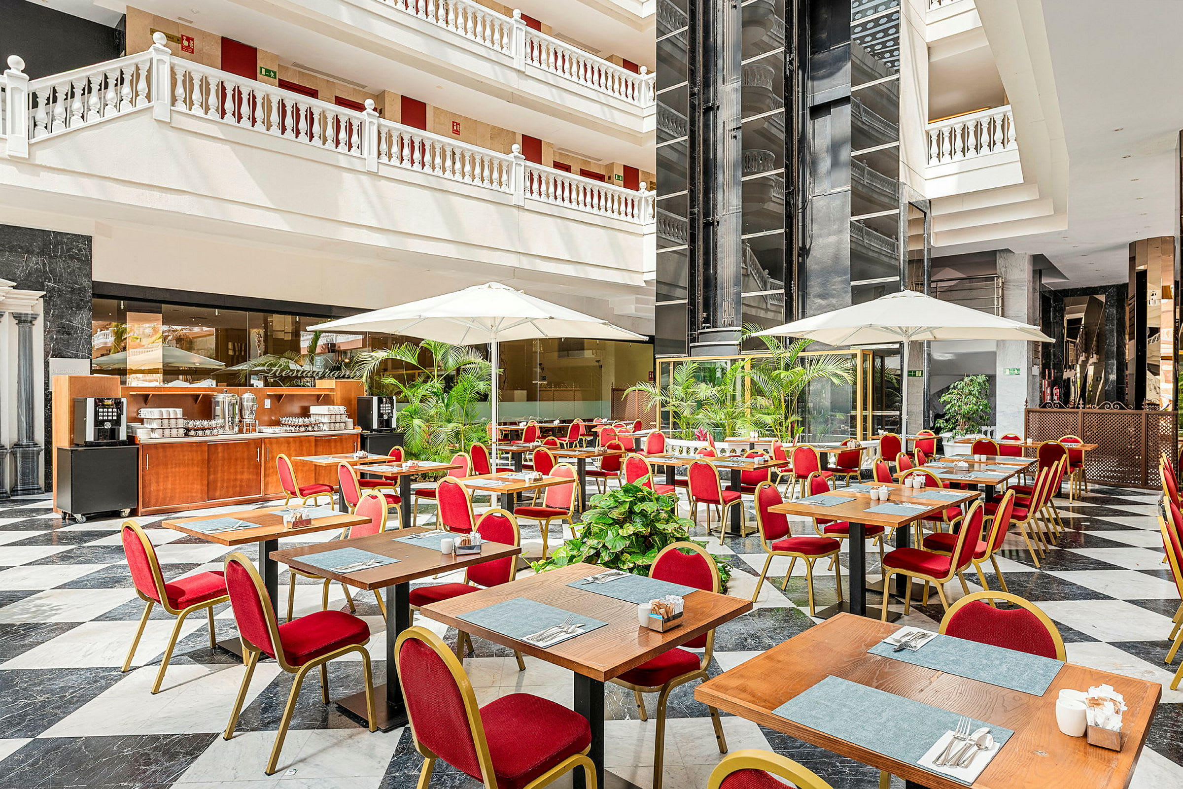 En restaurang med bord, röda stolar och parasoller i ett ljust atrium. (AI-genererad text)