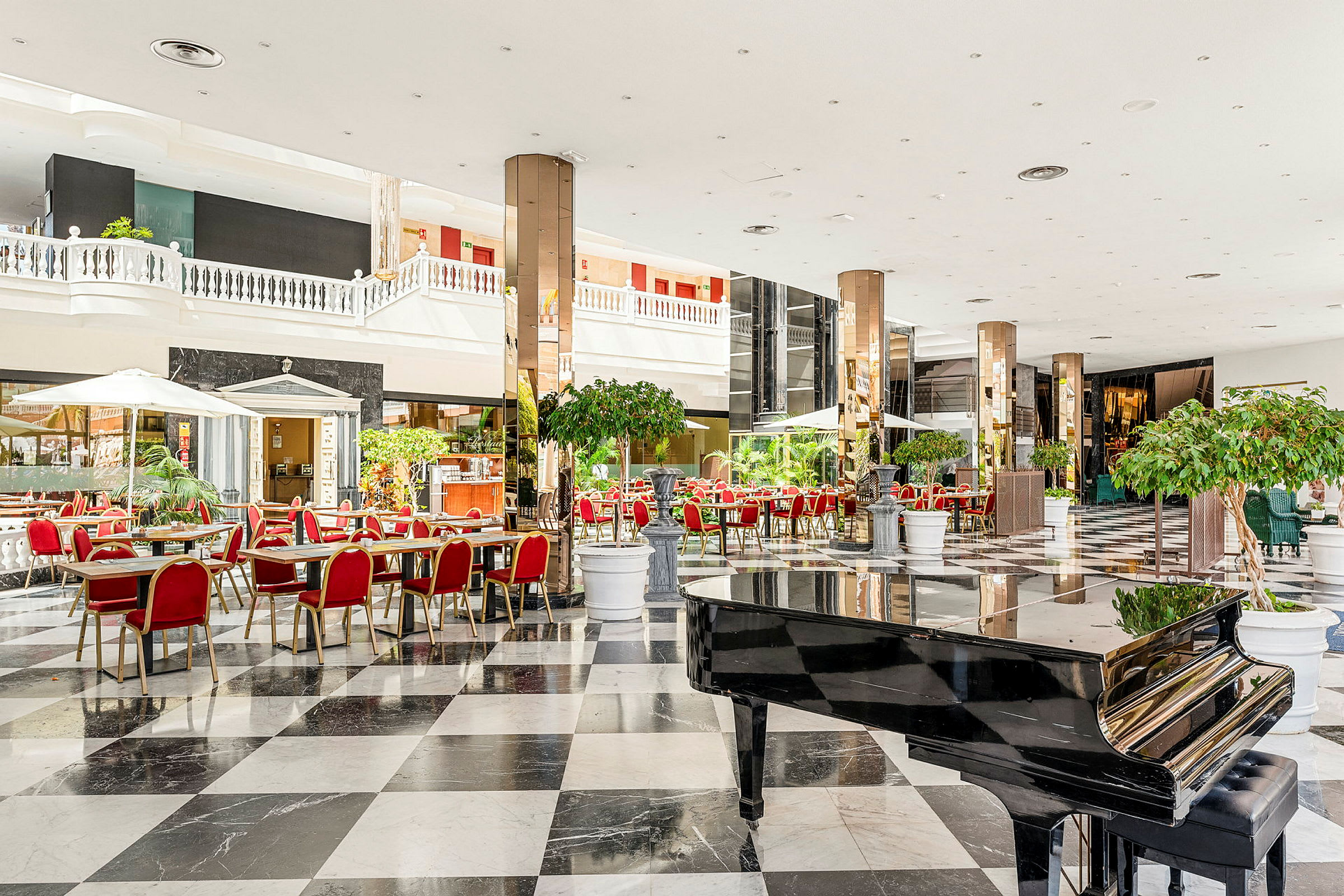 En rymlig hotellobby med svarta och vita rutiga golv, röda stolar och ett svart piano. (AI-genererad text)