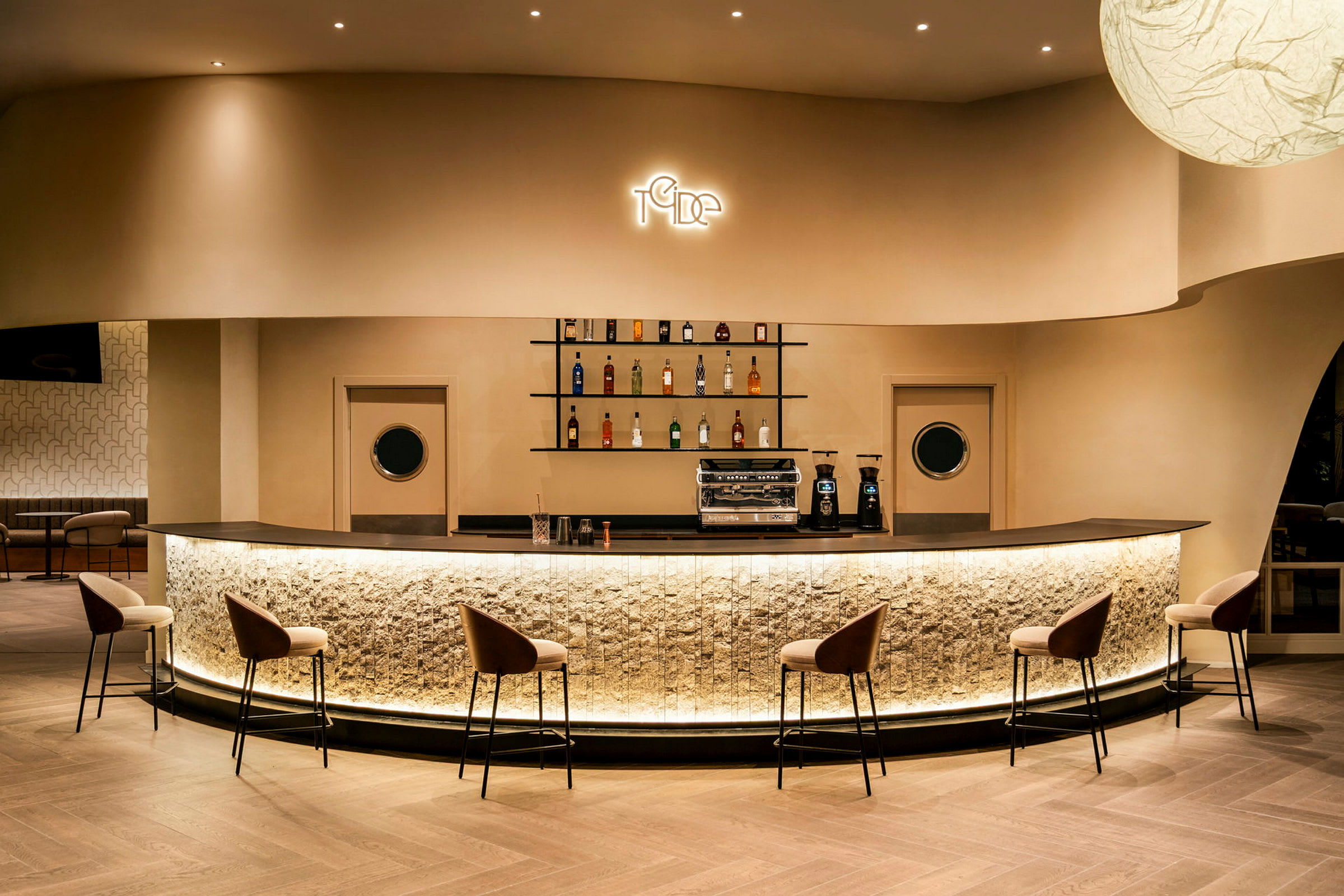 En modern bar med upplyst bardisk, barstolar och hyllor med flaskor. (AI-genererad text)
