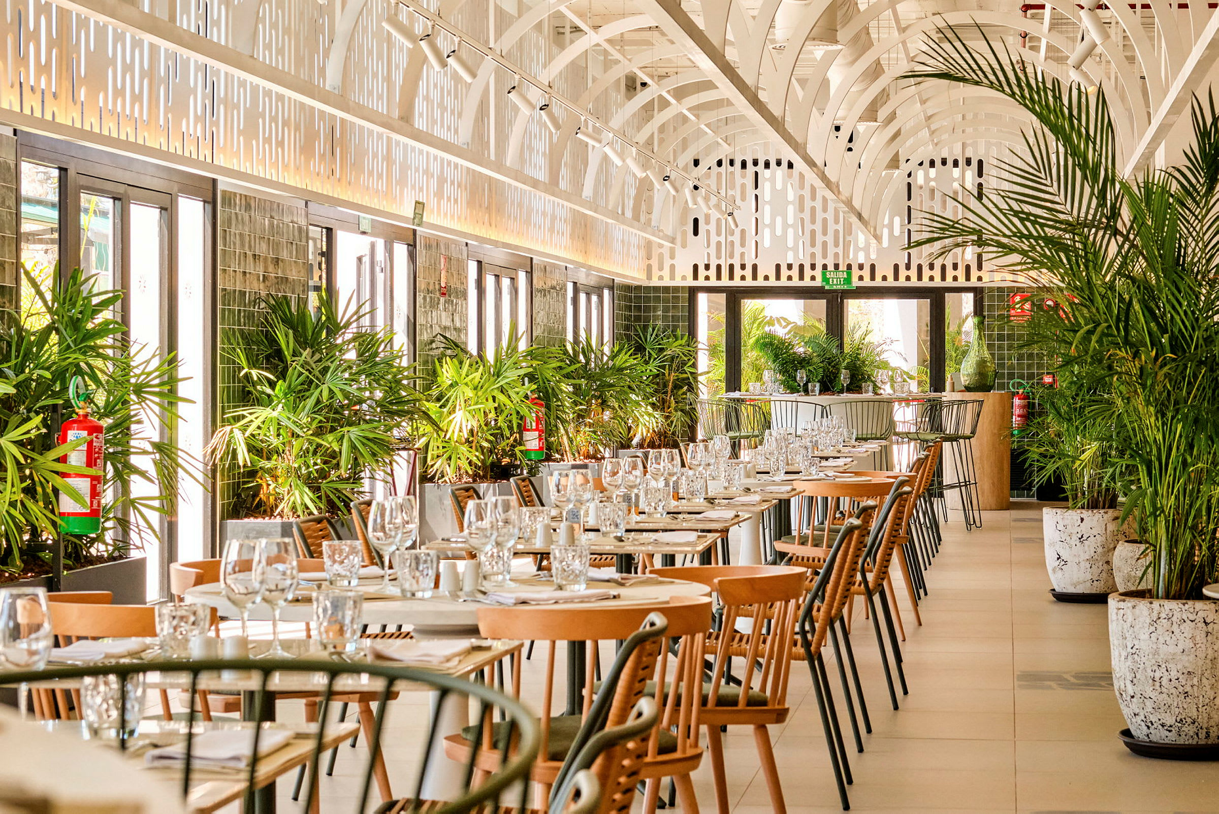 En restaurang med uppställda bord och stolar, dekorerad med gröna växter. (AI-genererad text)