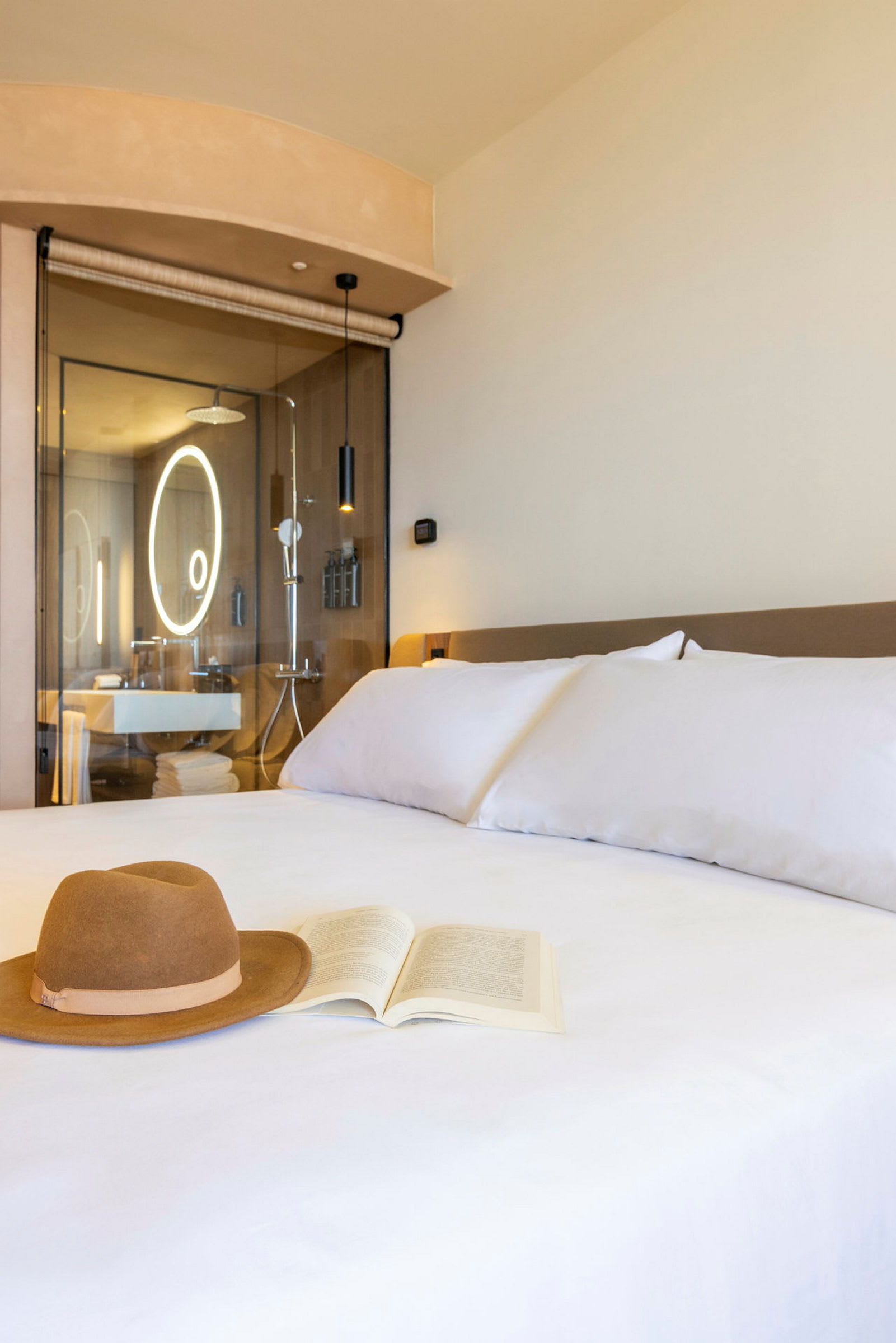 En hotellrumsmiljö med en säng där en hatt och en bok ligger. I bakgrunden syns ett modernt badrum. (AI-genererad text)