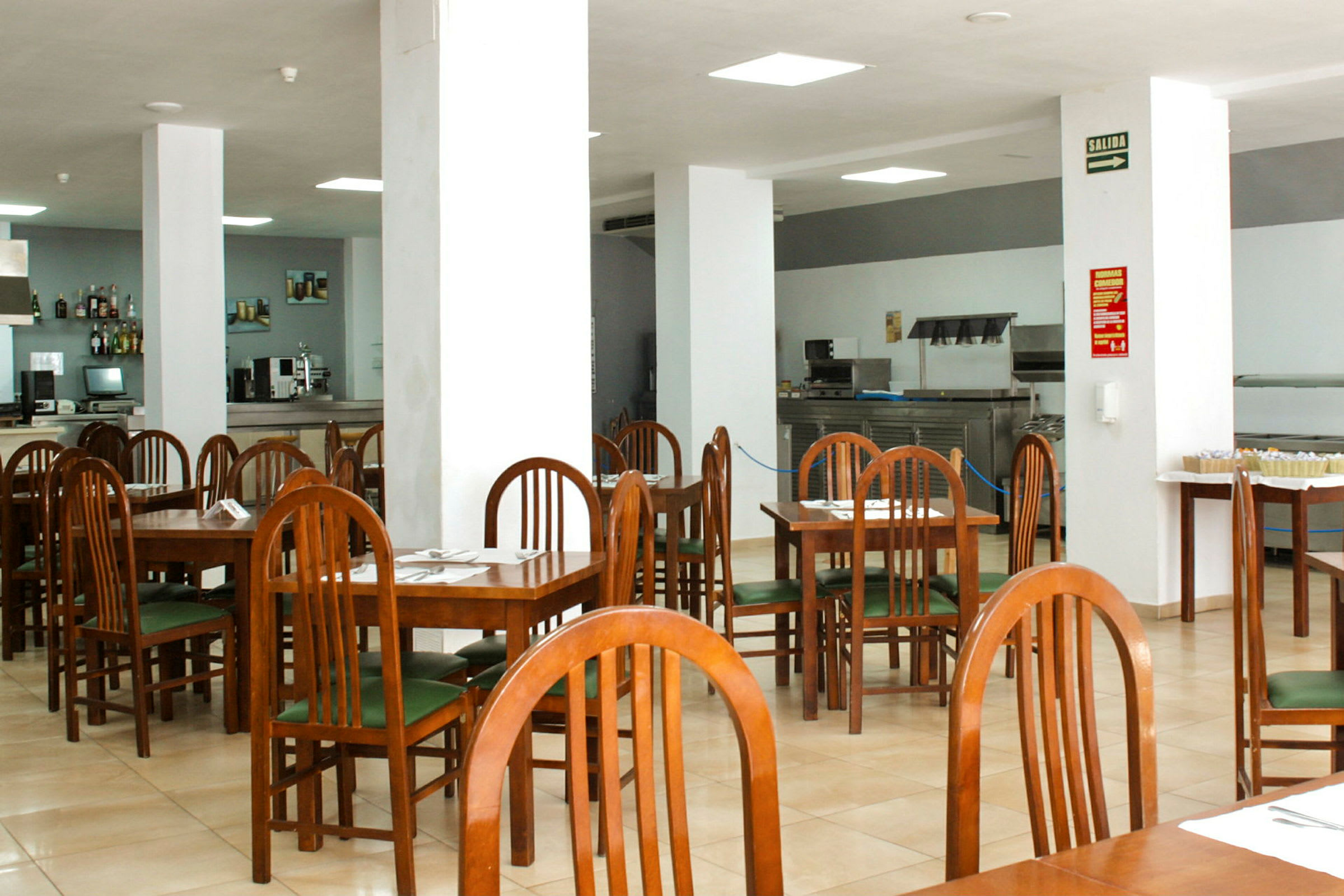 Ett kafé eller restaurang med trästolar och bord samt vita pelare i ett stort öppet utrymme. (AI-genererad text)