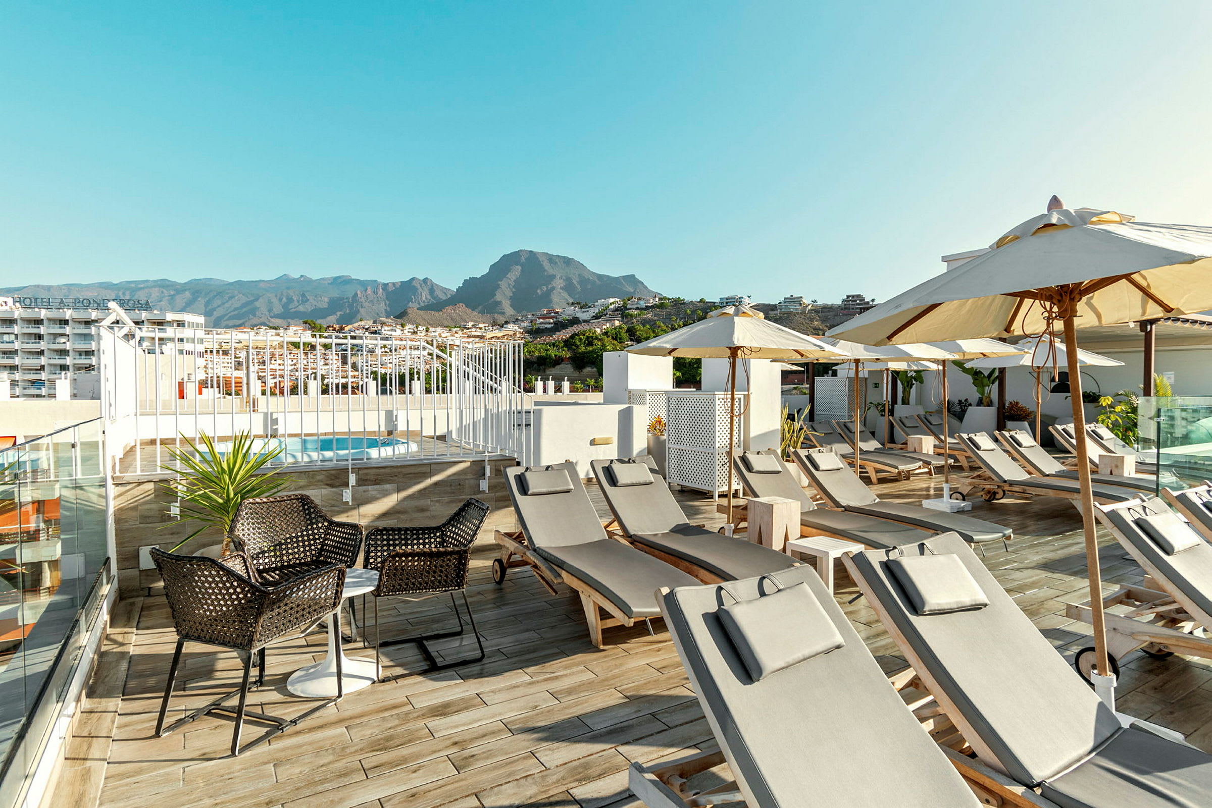 Pool med solstolar och parasoller på en hotellterrass med berg i bakgrunden. (AI-genererad text)