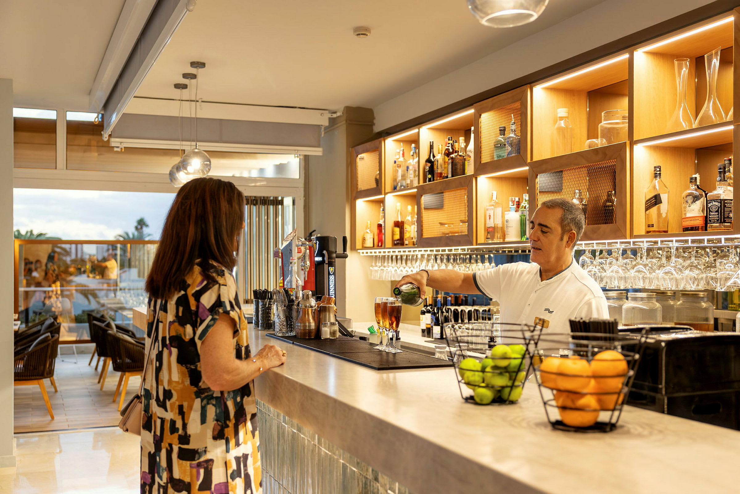 En kvinna som står vid en bar där en bartender häller upp en dryck. (AI-genererad text)