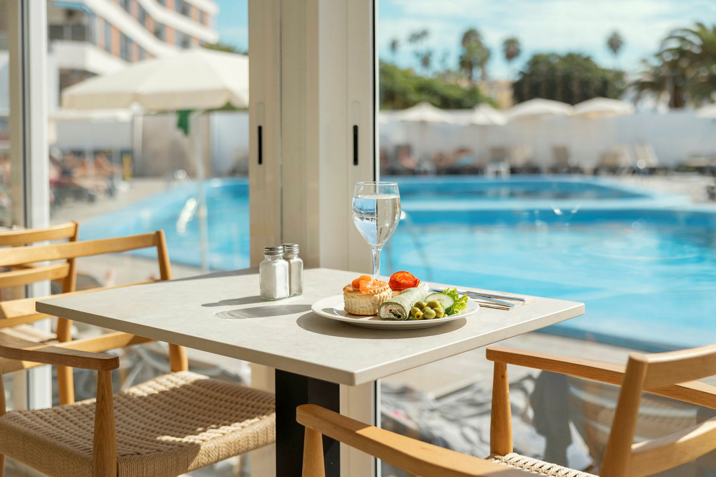 Ett dukat bord med en tallrik mat och ett glas vatten vid en pool. (AI-genererad text)