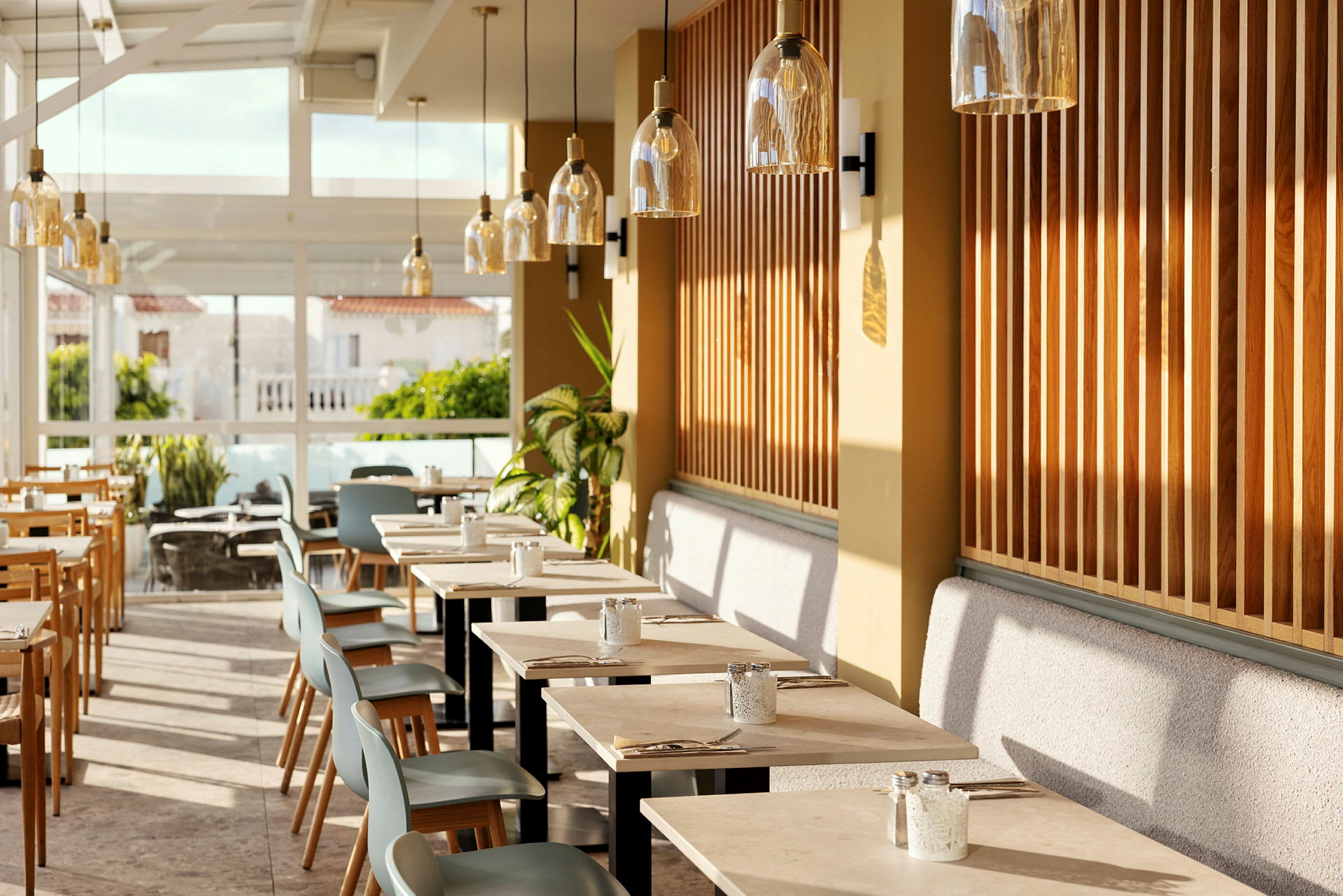 En restauranginteriör med moderna bord och stolar, omgiven av stora fönster och växter. (AI-genererad text)