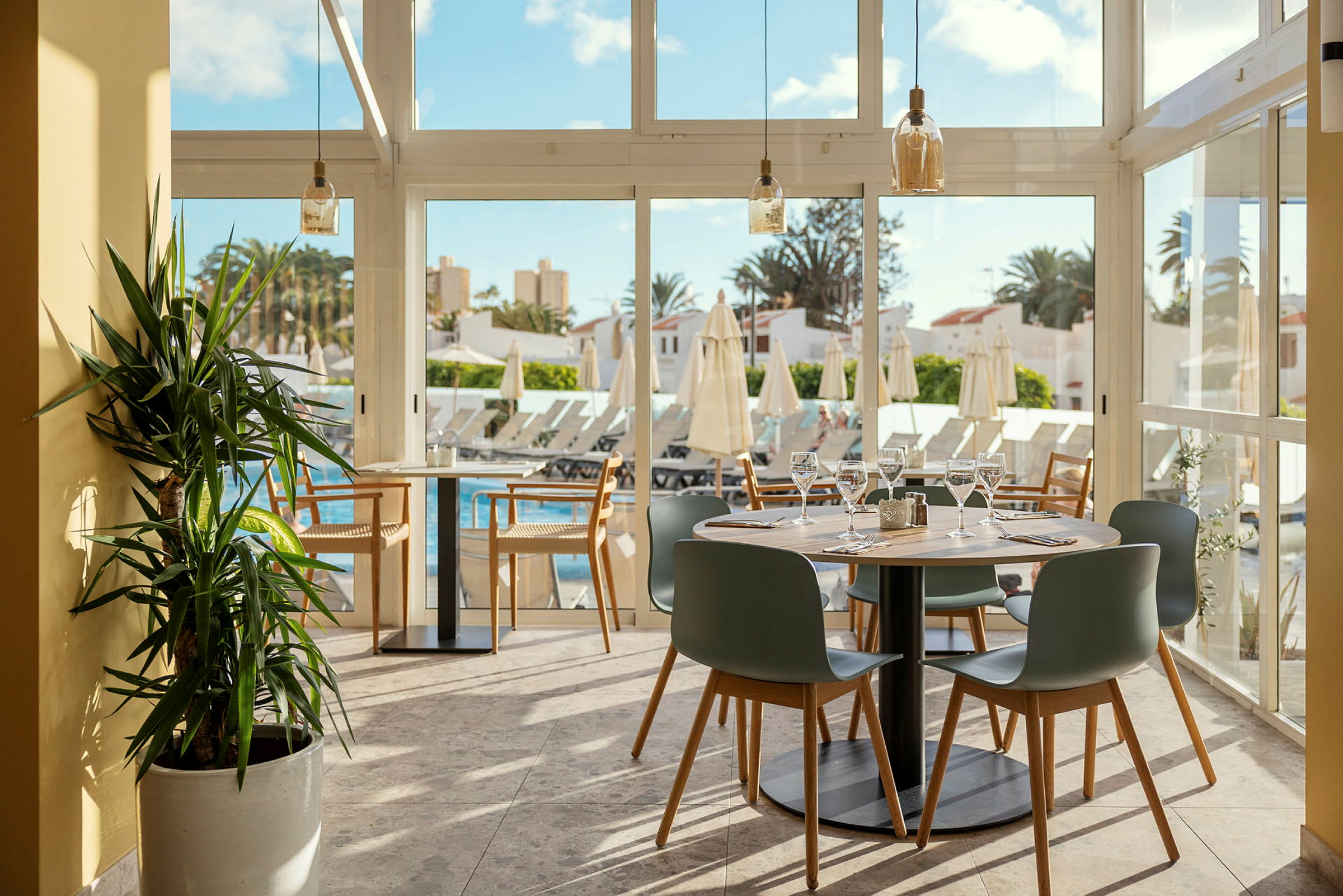 Restaurang med dukade bord och utsikt över pool och solstolar. (AI-genererad text)