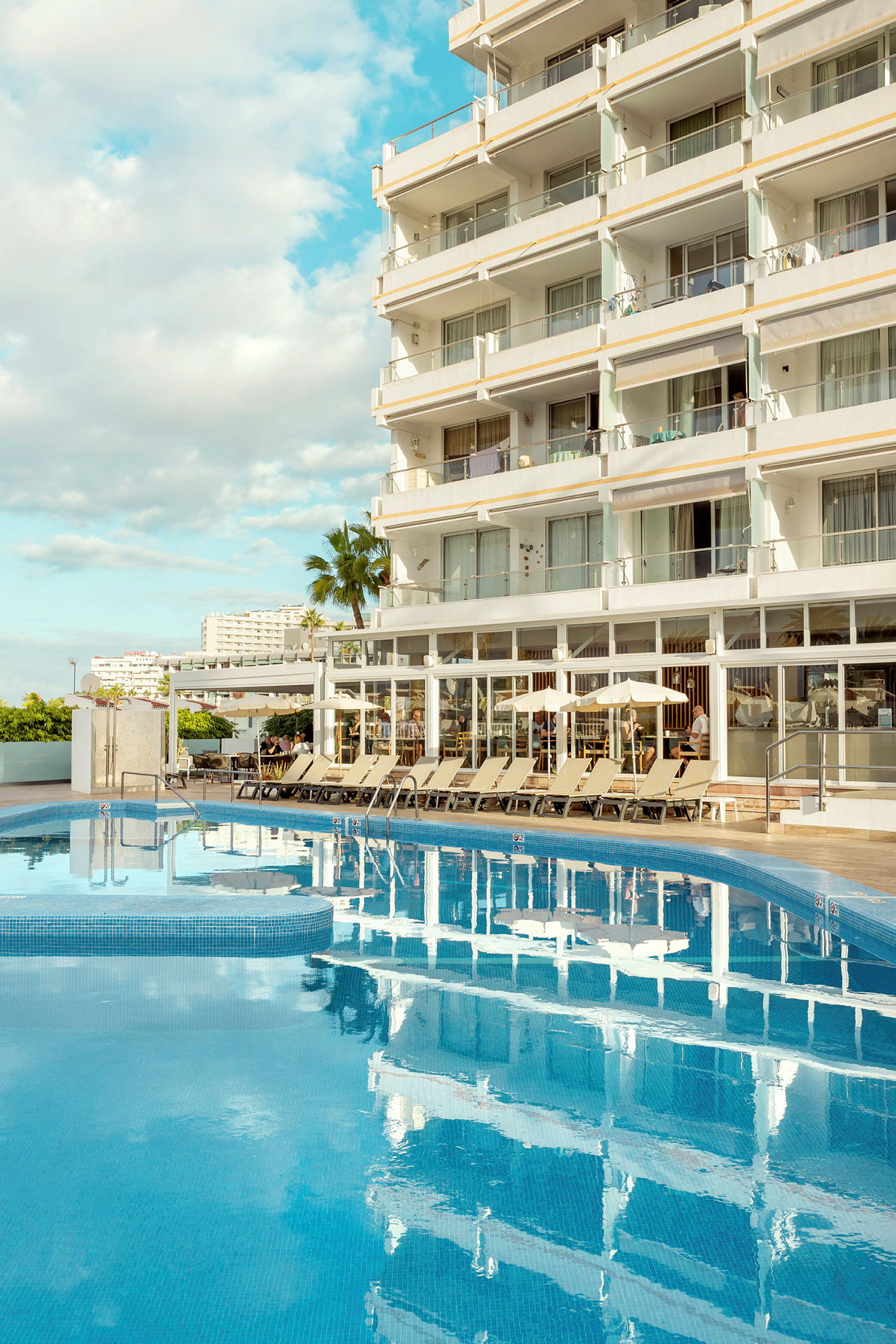 Ett hotell vid en pool med solstolar runtom. (AI-genererad text)