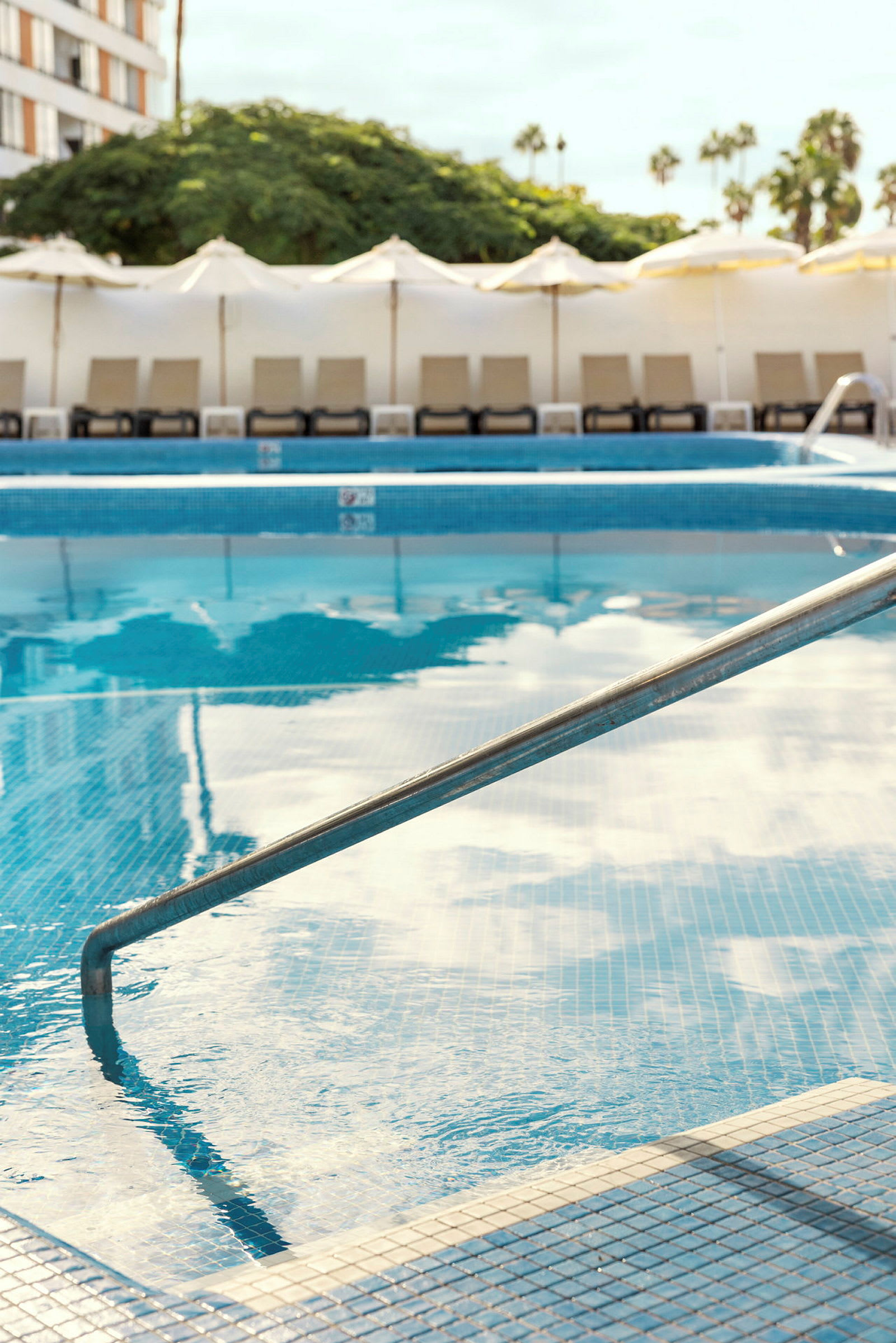 En pool med räcke och skuggor av paraplyer och palmer. (AI-genererad text)