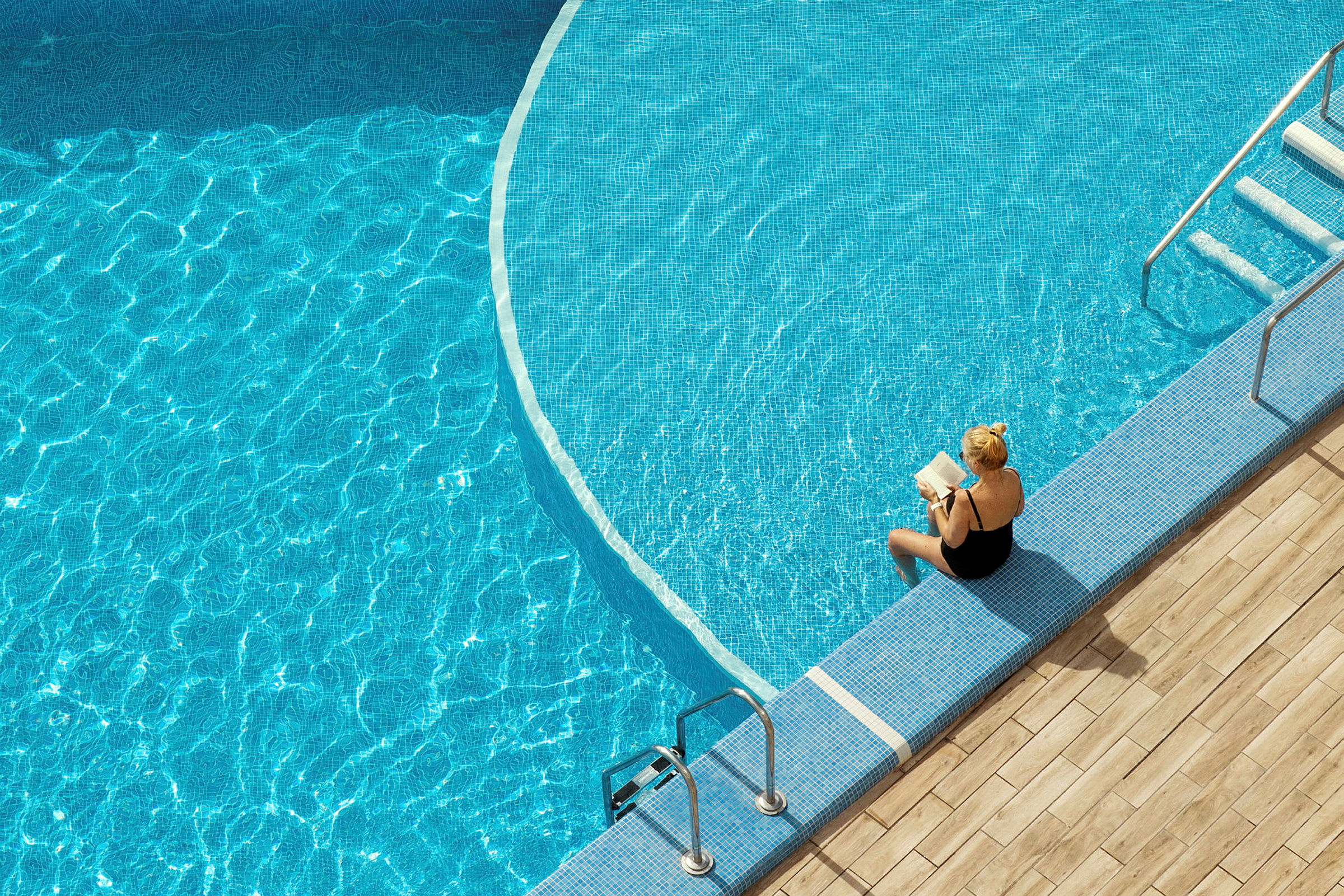 En person sitter vid kanten av en pool och läser en bok. (AI-genererad text)