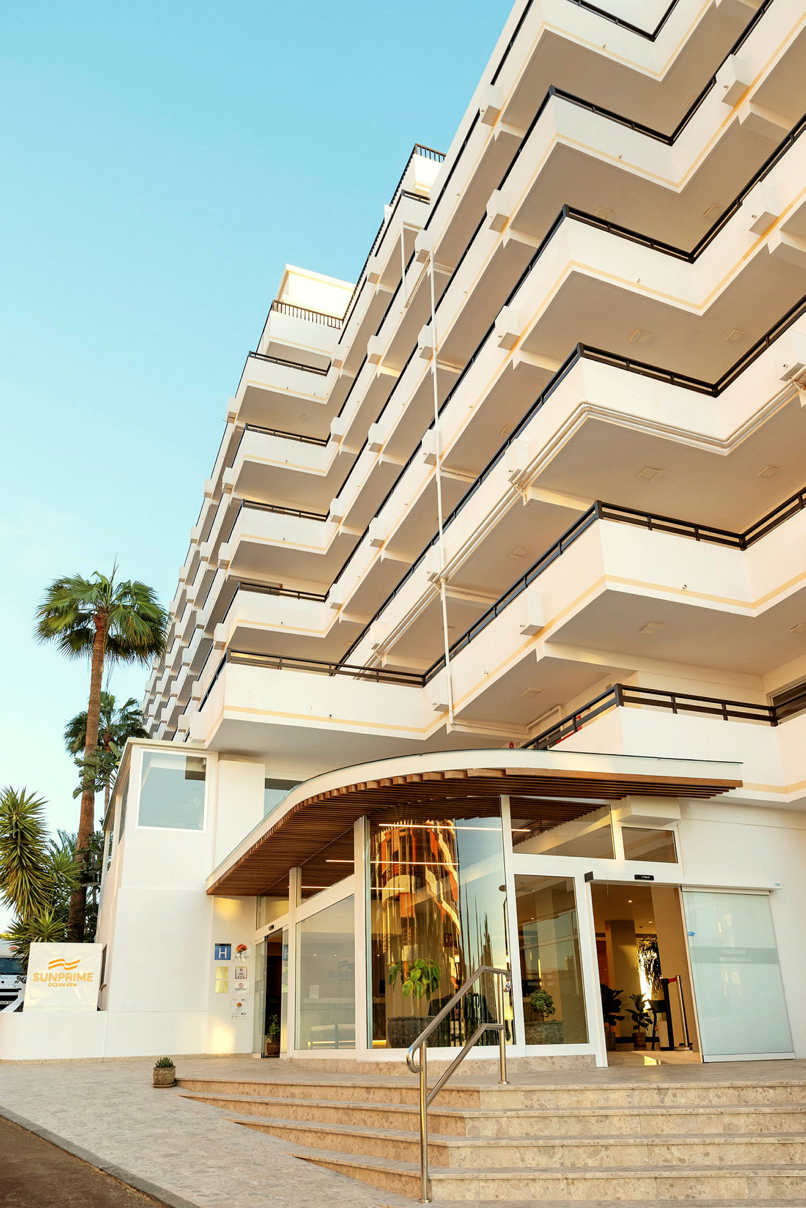 Hotellbyggnad med flera våningar och balkonger, samt en entré med glasdörrar. (AI-genererad text)