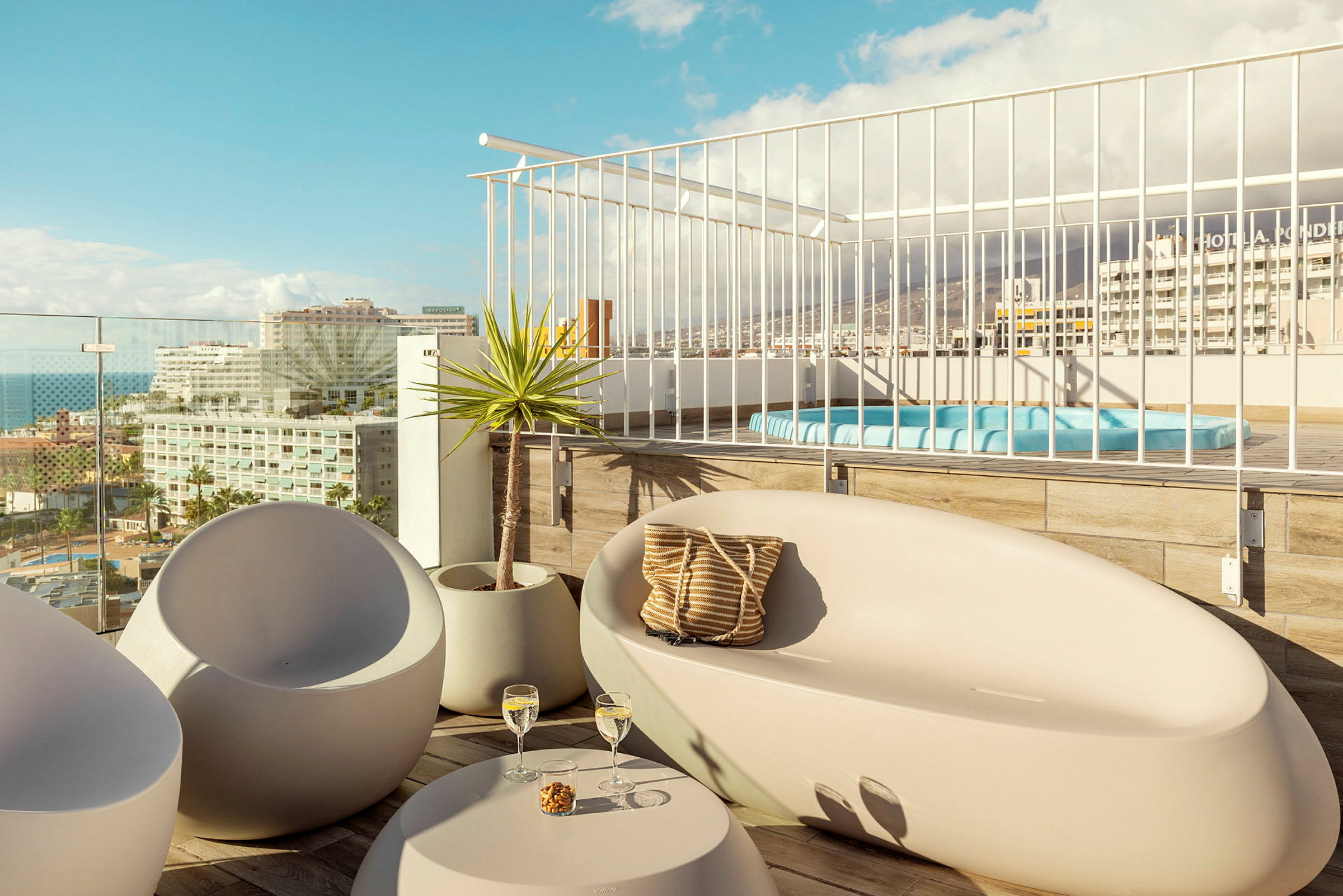Utsikt över en möblerad terrass med sittplatser och jacuzzi, samt staden i bakgrunden. (AI-genererad text)