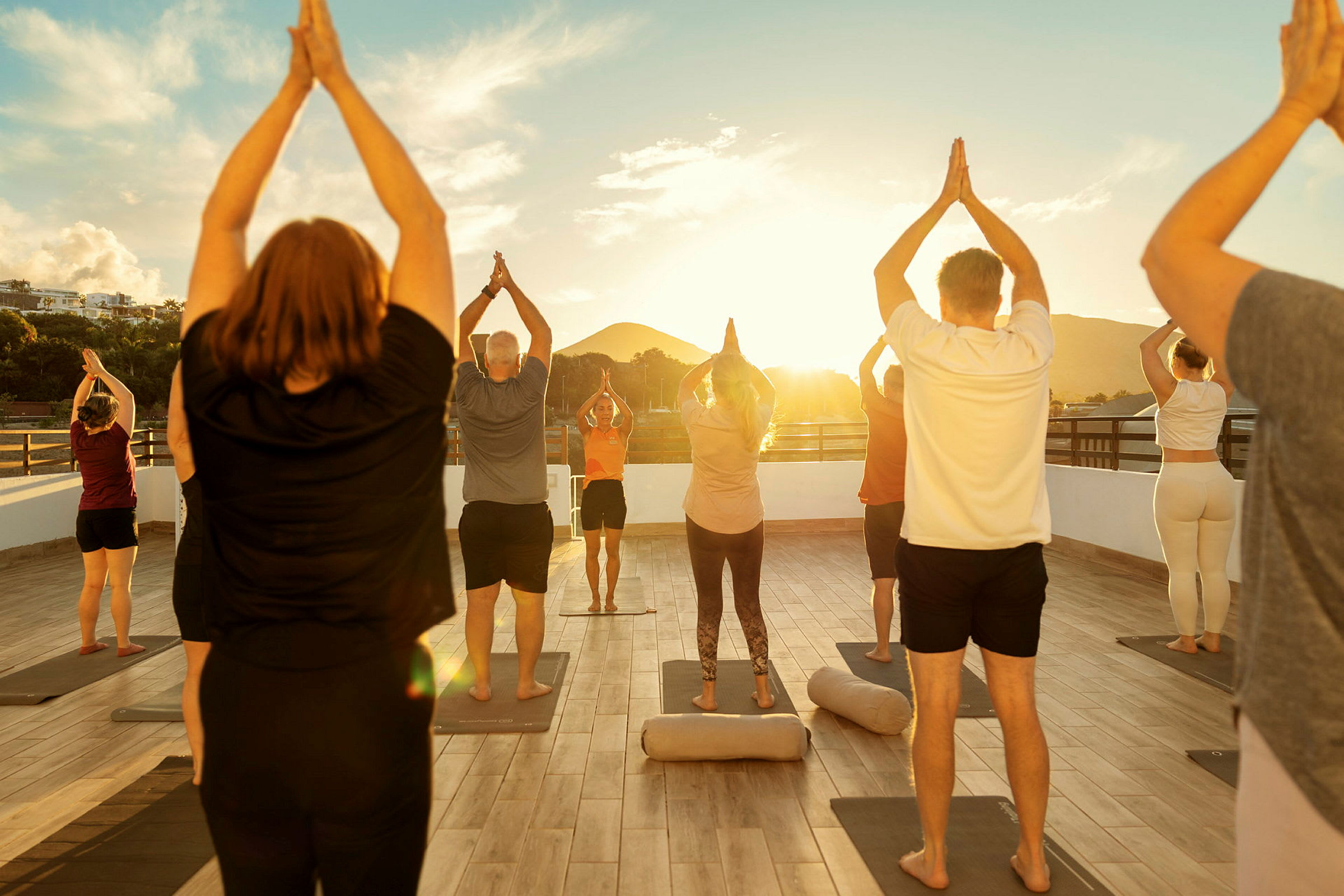 En grupp människor utför yogapositioner på en utomhusplattform vid solnedgången. (AI-genererad text)