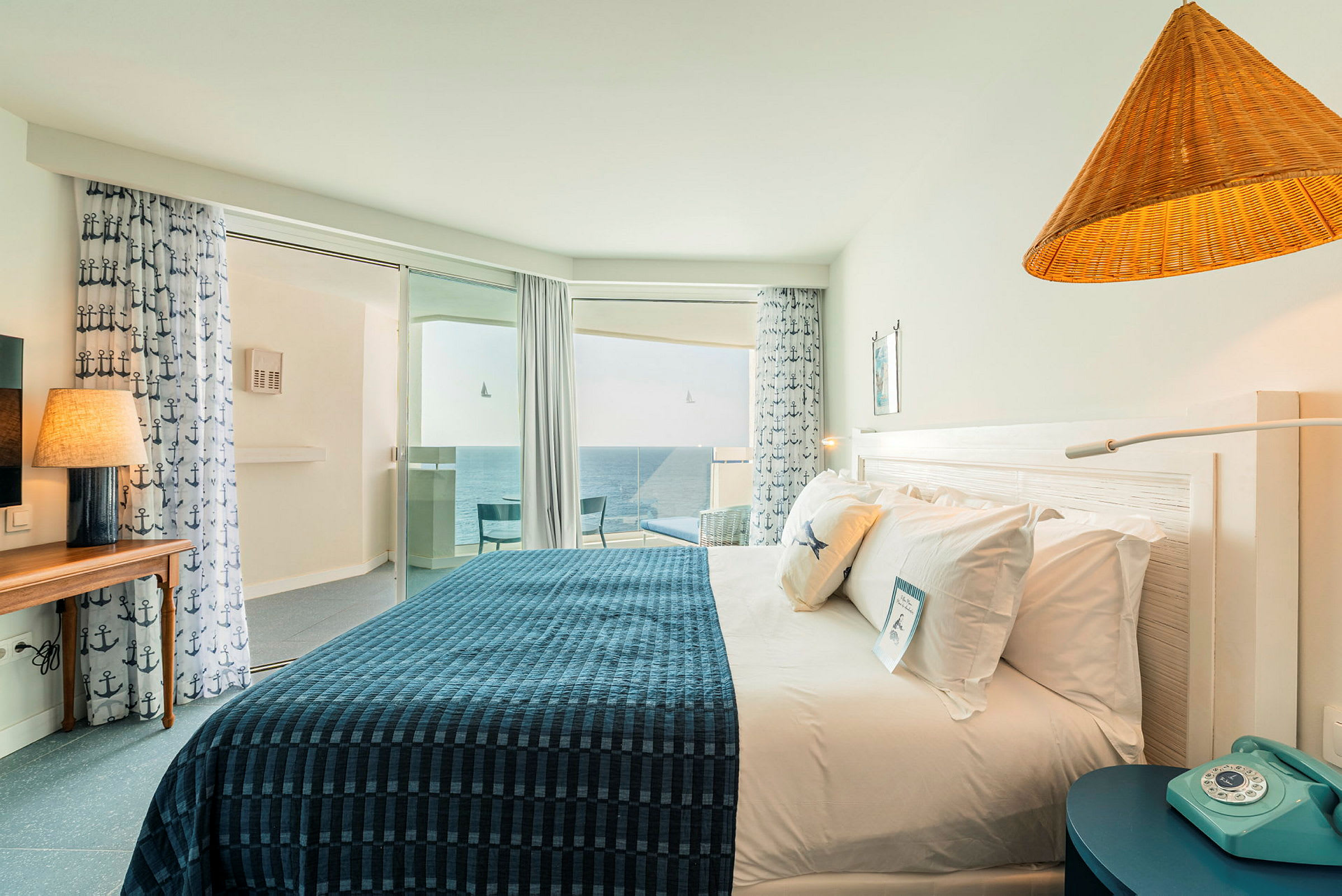 Ett hotellrum med en dubbelsäng, dekorationer i marint tema och ett fönster med utsikt över havet. (AI-genererad text)
