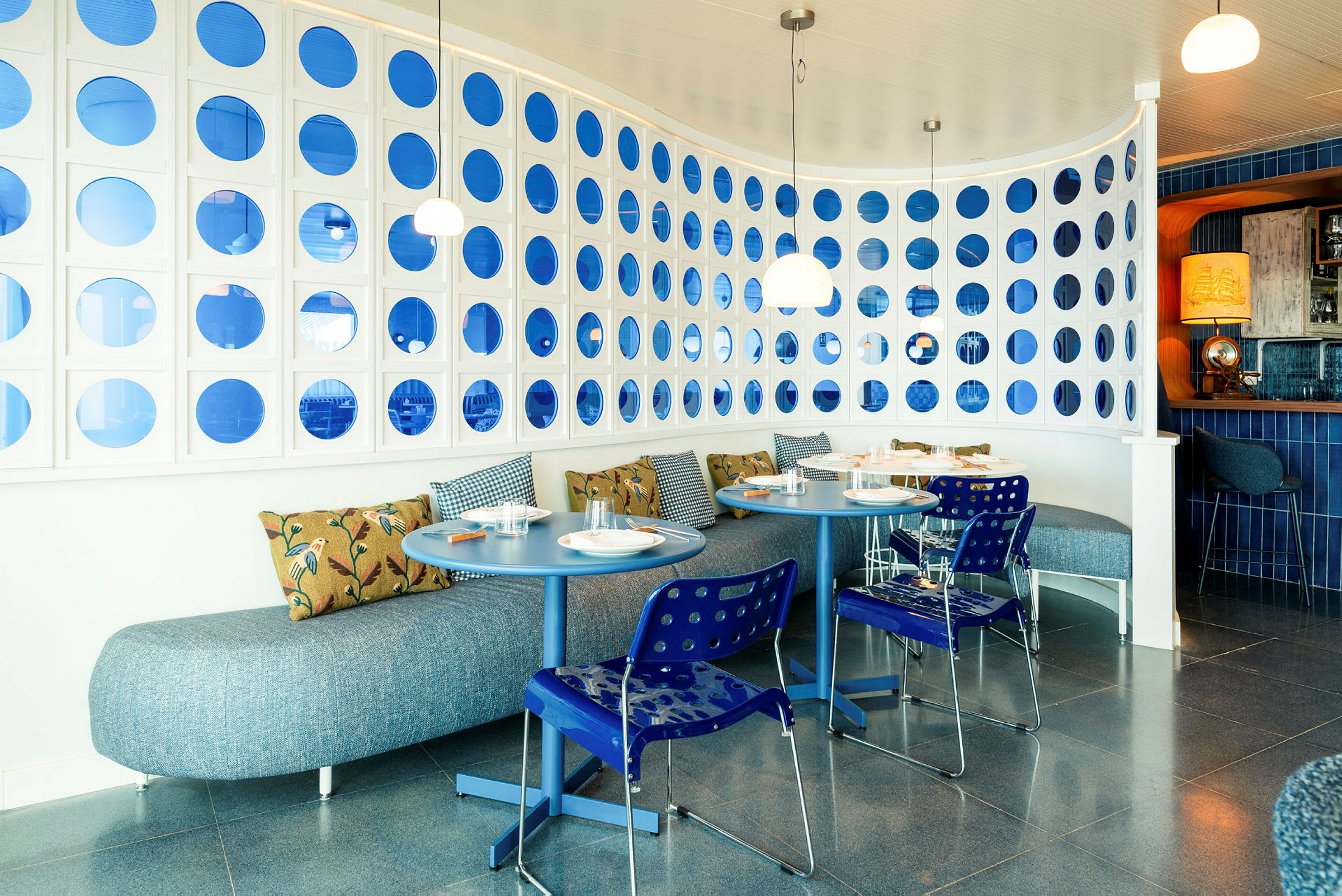 Ett modernt restaurangområde med blå och vita detaljer och runda bord. (AI-genererad text)