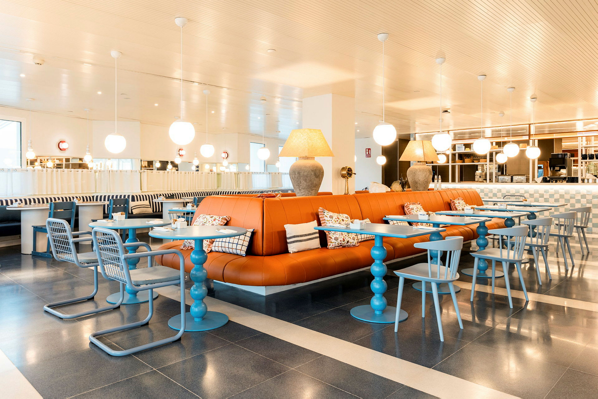 Ett modernt inrett kafé med orange lädersoffor, blå bord och stolar samt dekorativa lampor i taket. (AI-genererad text)