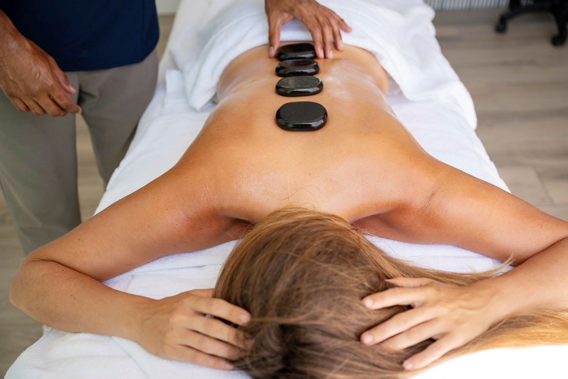 Massage utförs med varma stenar placerade på en kvinnas rygg. (AI-genererad text)