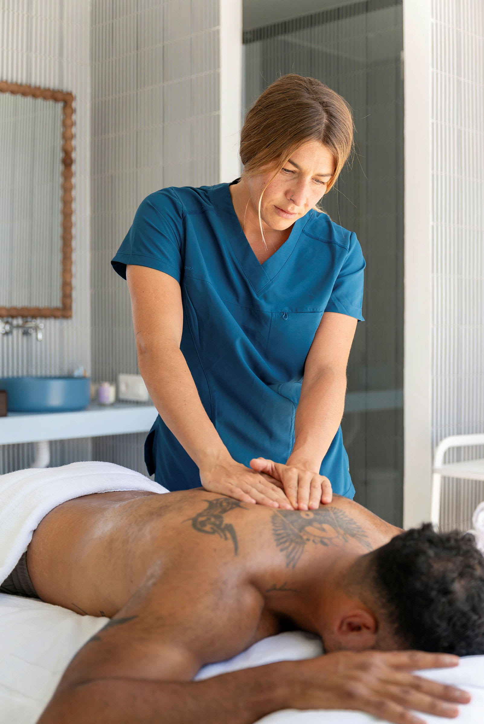 En person får en ryggmassage av en massör som bär blå arbetskläder. (AI-genererad text)