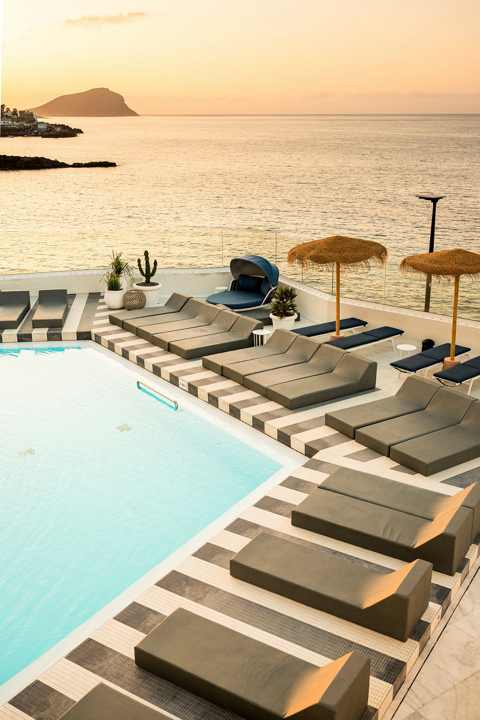 Poolområde med solbäddar och utsikt över havet vid solnedgång. (AI-genererad text)