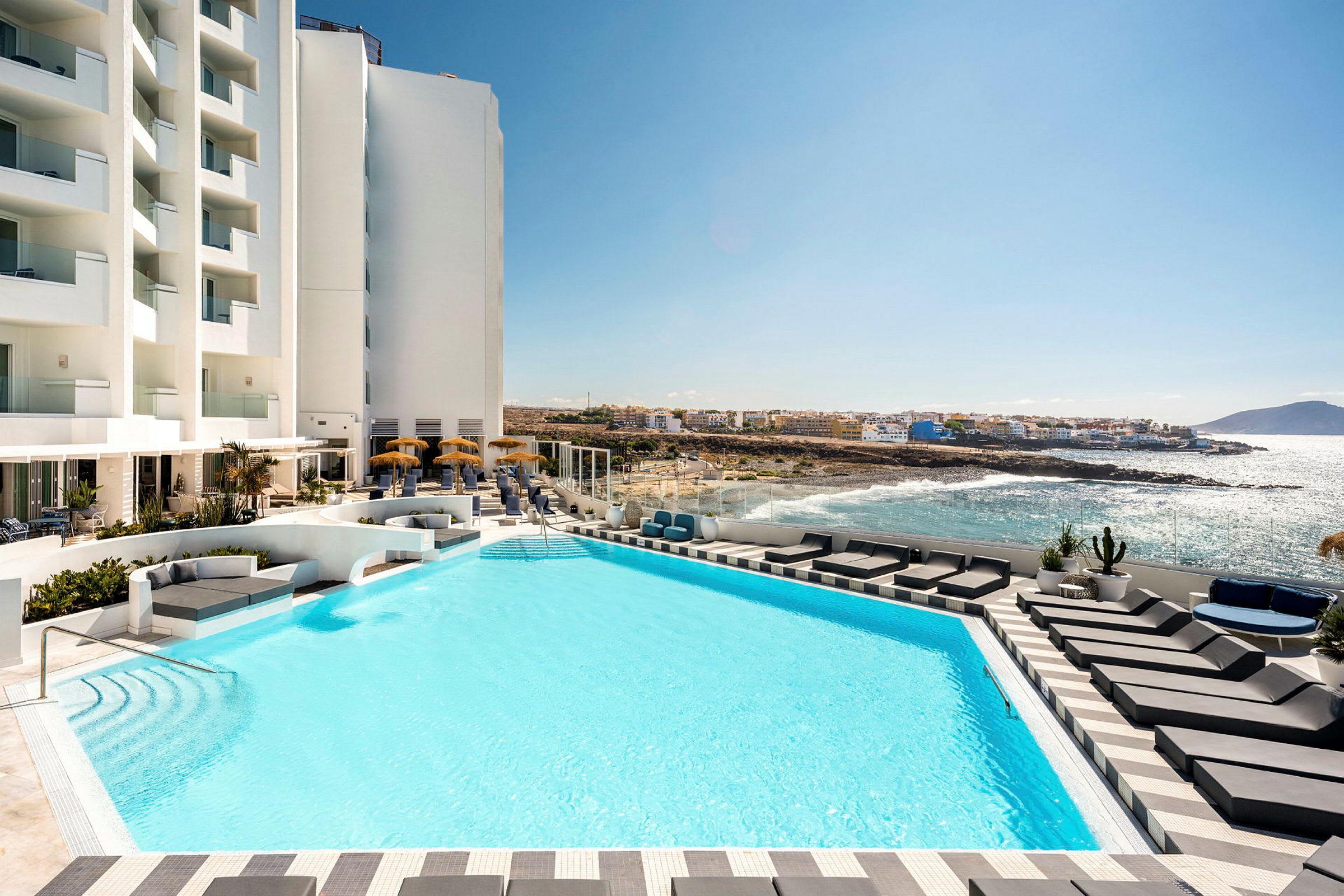 Hotellets poolområde med solstolar och utsikt över havet. (AI-genererad text)
