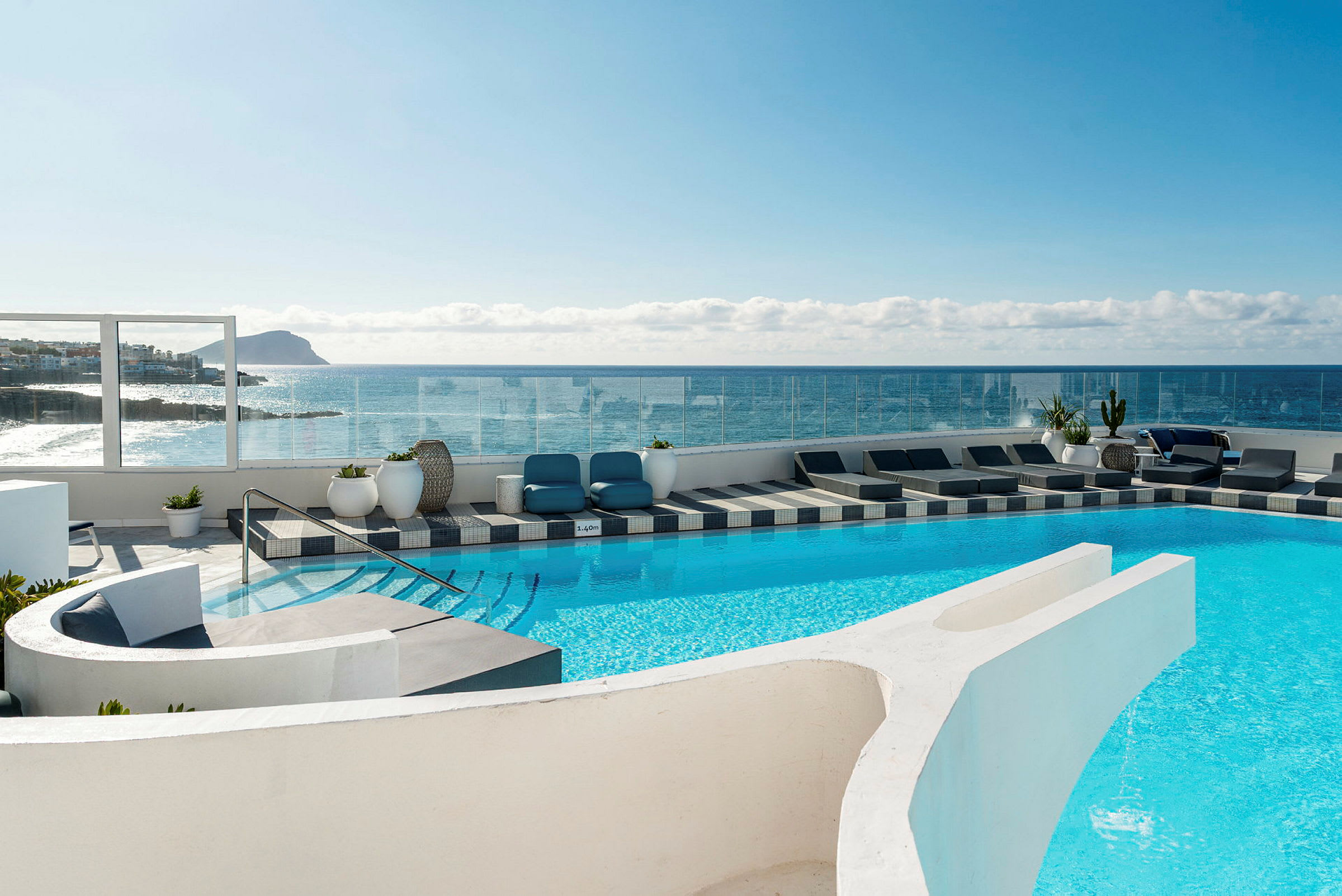En utomhuspool vid ett hotell med solstolar och utsikt över havet och en klippig kust. (AI-genererad text)