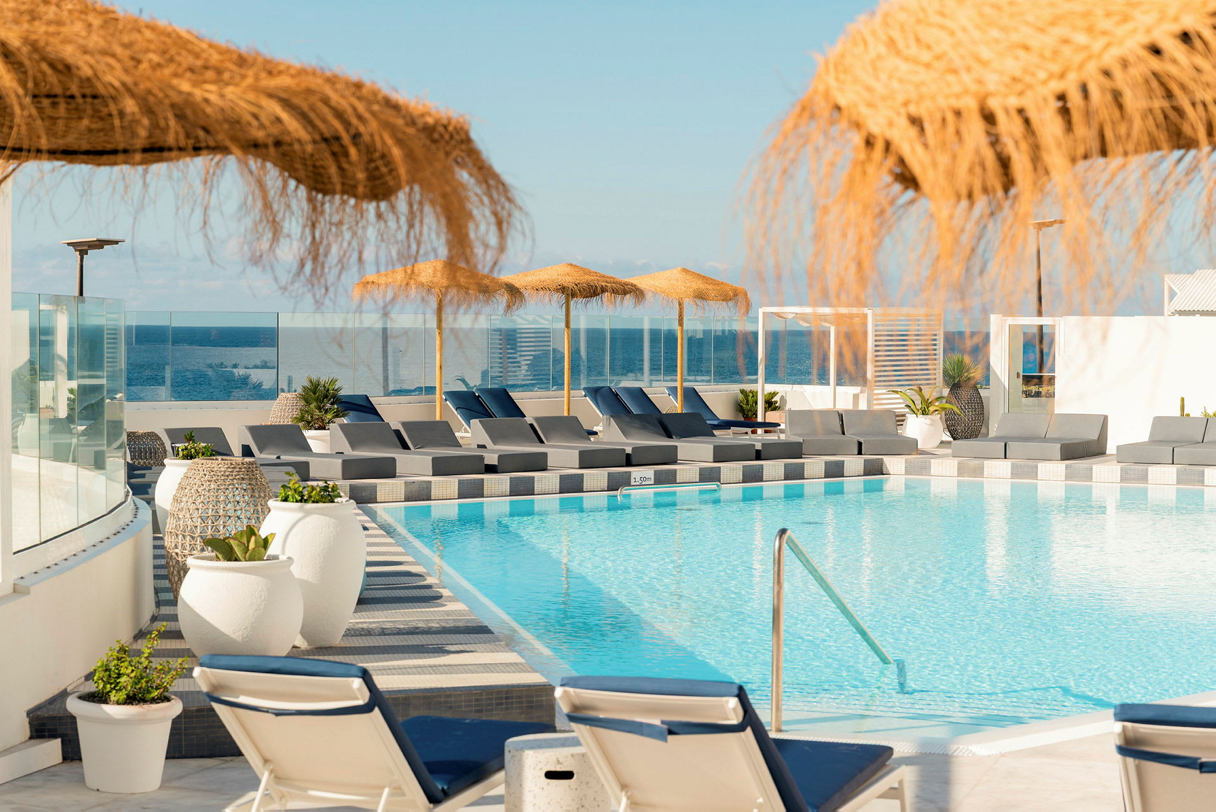 En pool med solstolar och parasoller, med utsikt mot havet. (AI-genererad text)