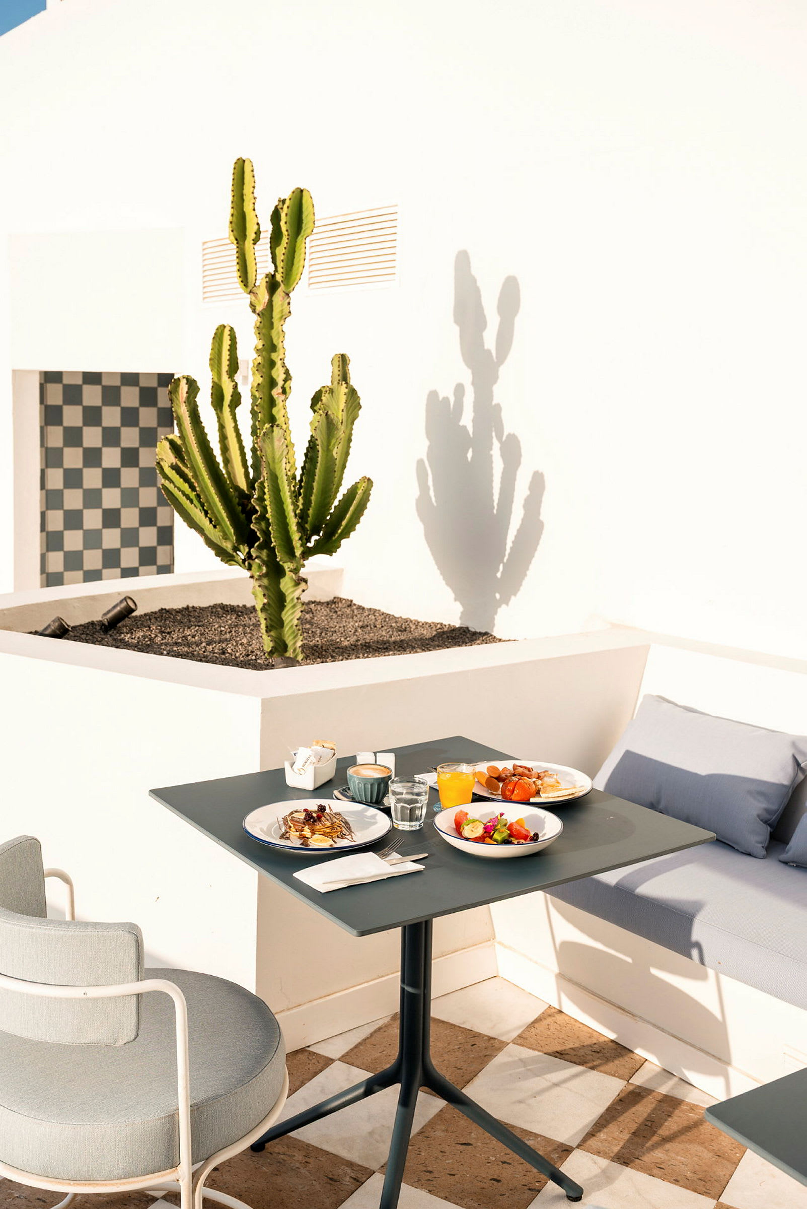 Ett bord med frukostuppsättning på en terrass med en kaktus i bakgrunden. (AI-genererad text)