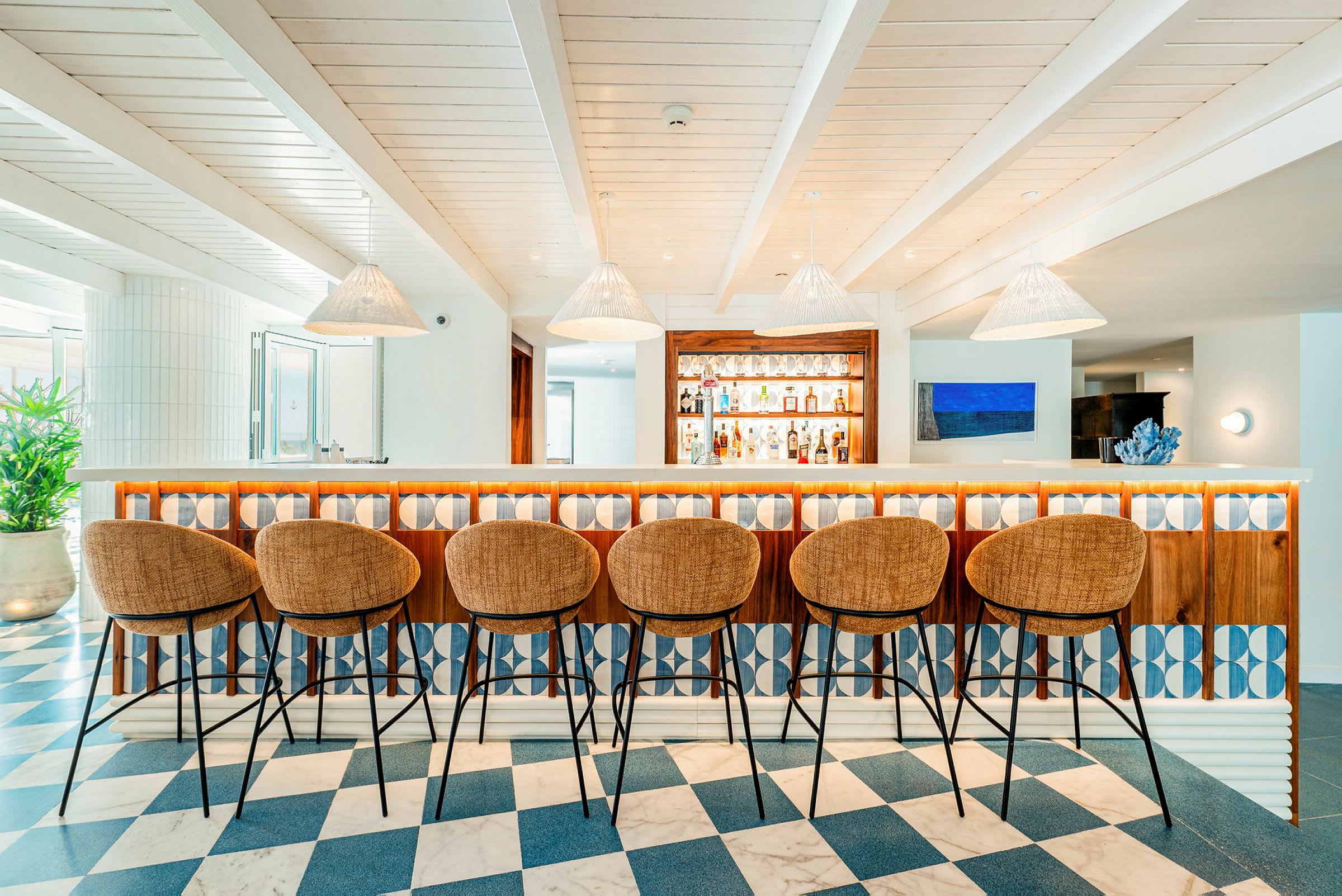 En modern bar med höga stolar och hängande lampor, med hyllor fyllda med flaskor i bakgrunden. (AI-genererad text)