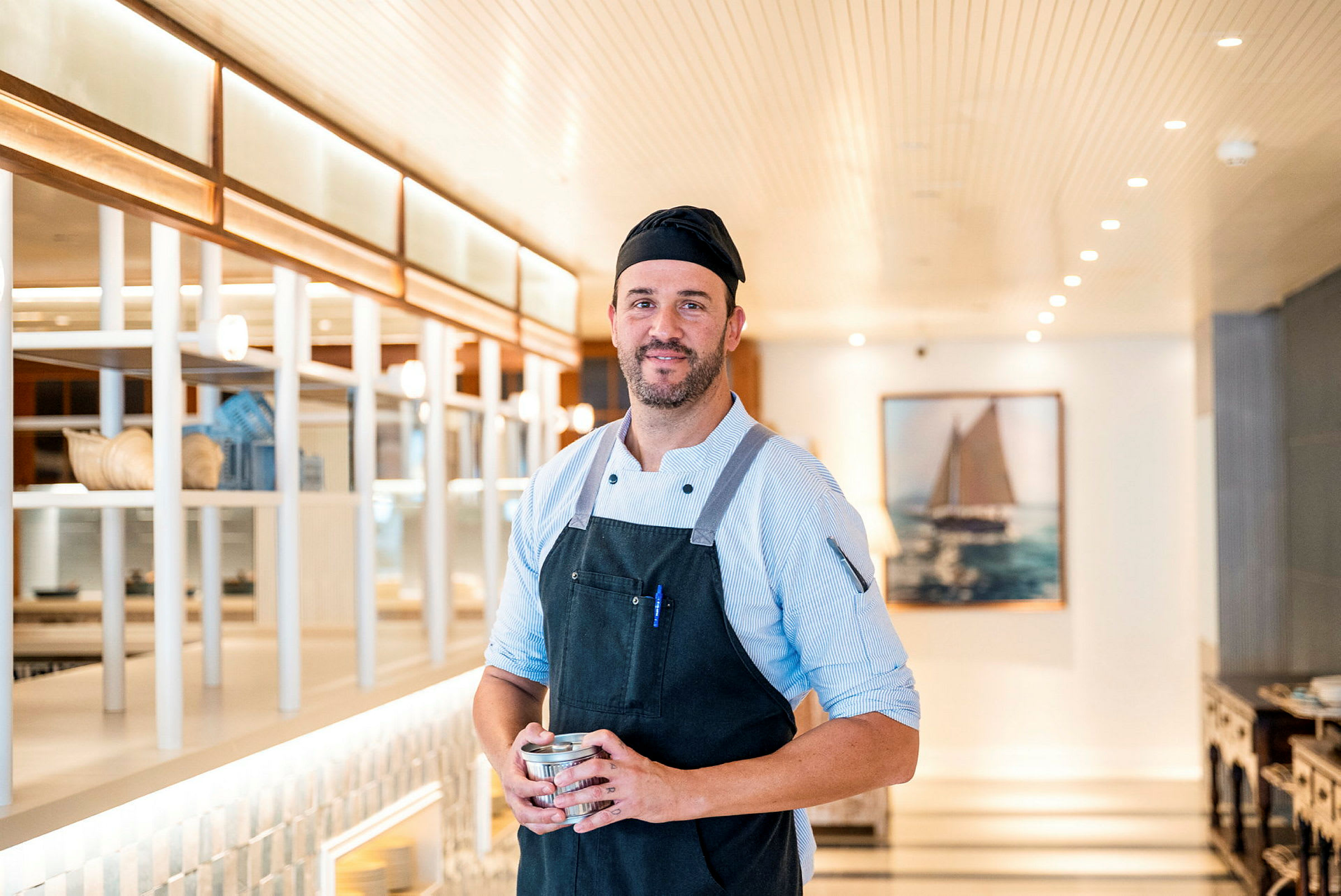 En kock i arbetskläder står i en ljus restaurangmiljö med modern inredning. (AI-genererad text)