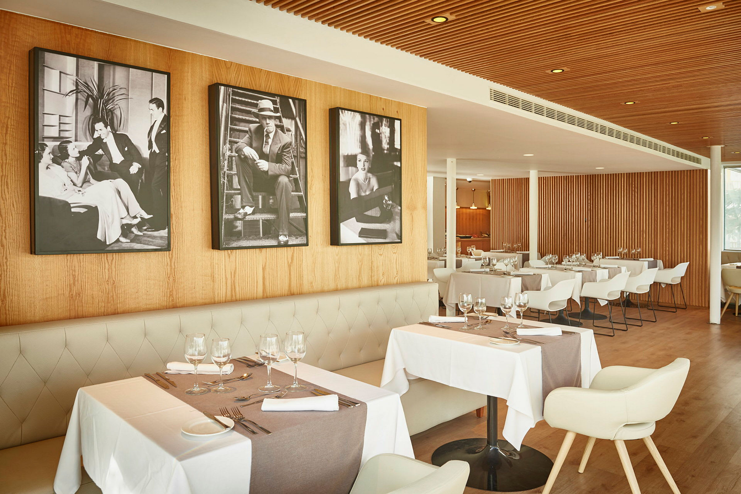 Interiör av en restaurang med bord dukade för gäster, väggar av träpanel och svartvita tavlor som dekoration. (AI-genererad text)