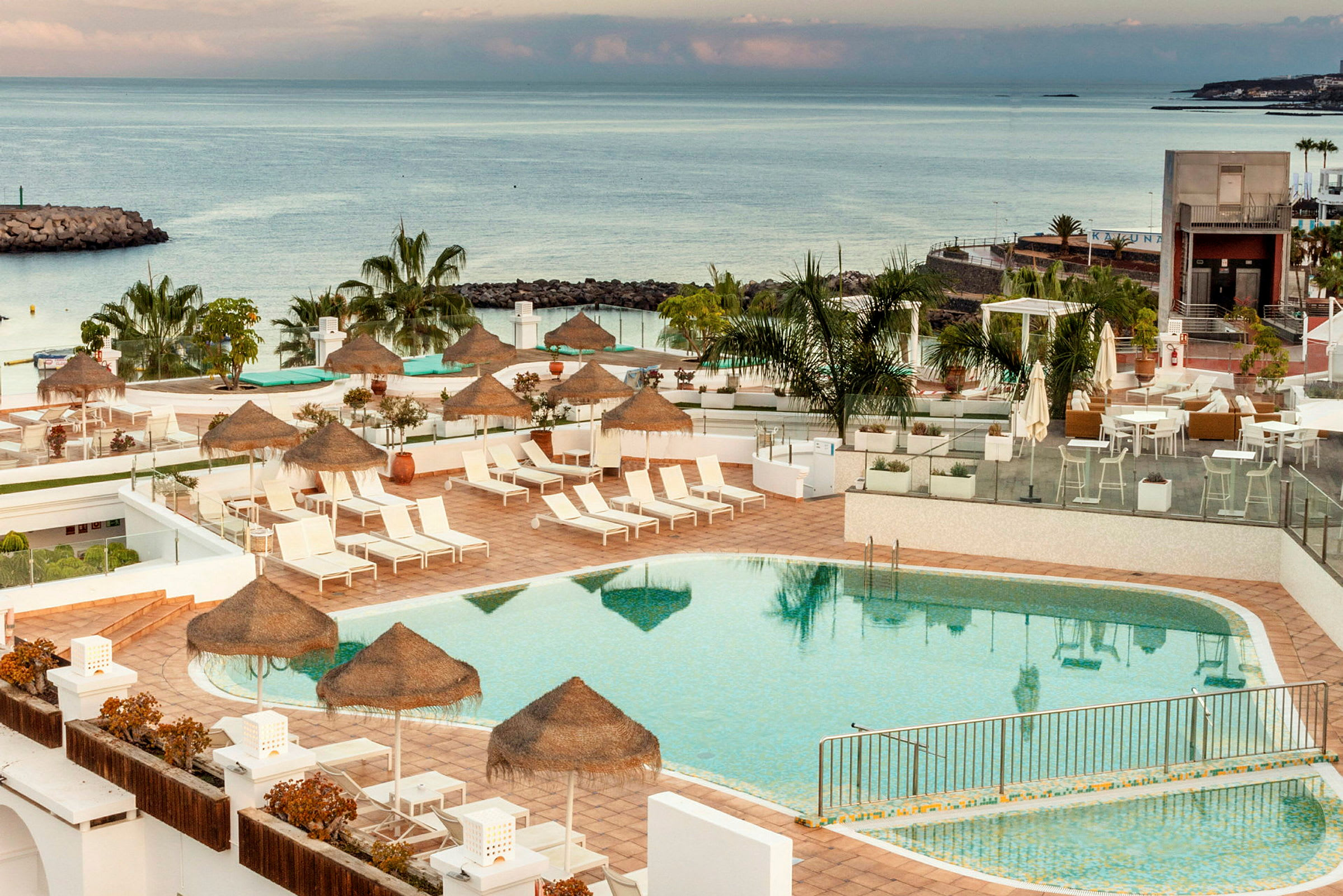 Bild av en utomhuspool vid ett hotell med solstolar och parasoll. Havet syns i bakgrunden. (AI-genererad text)