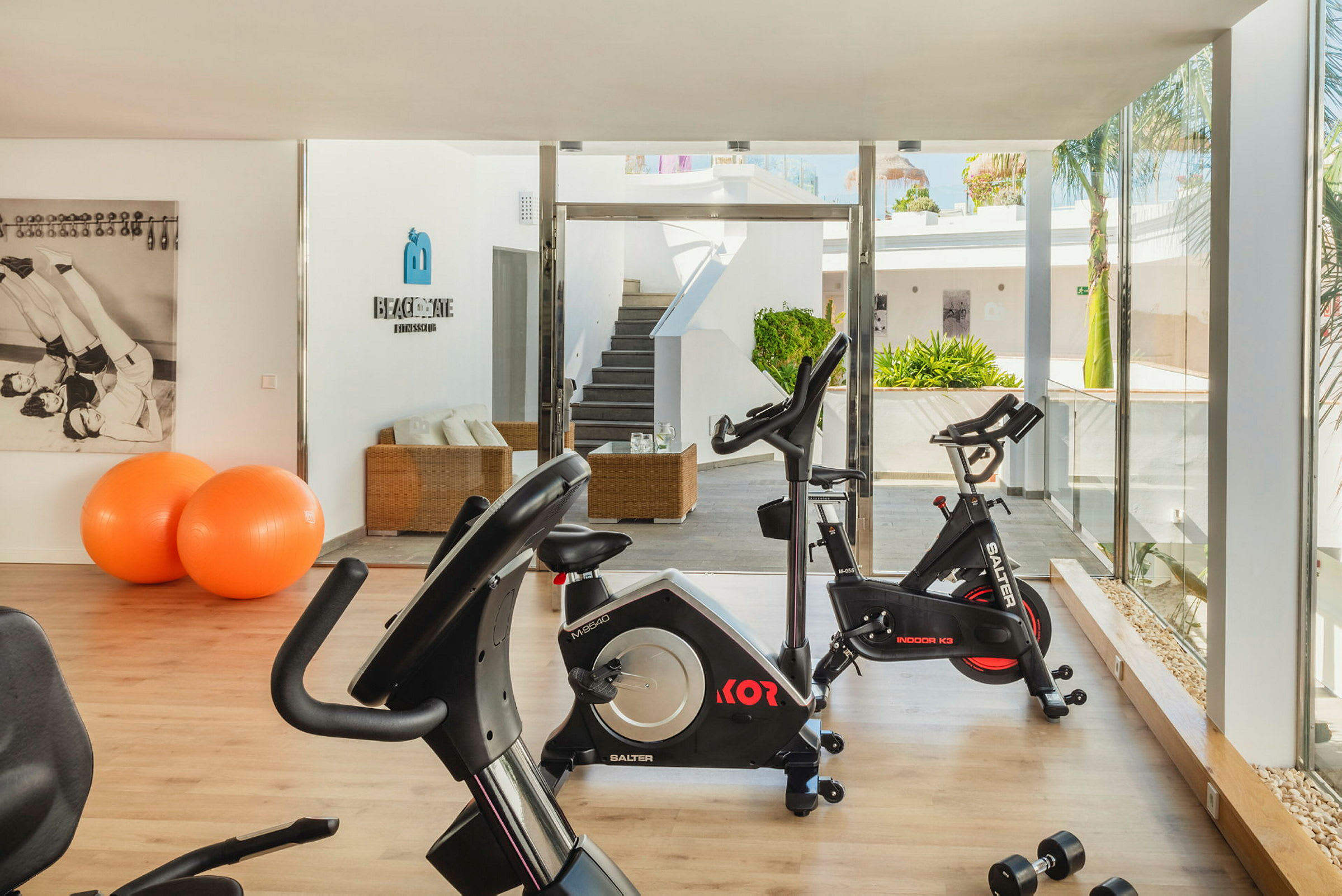 Ett modernt gym med träningscyklar och orange balansbollar. Ljus interiör och glasväggar. (AI-genererad text)