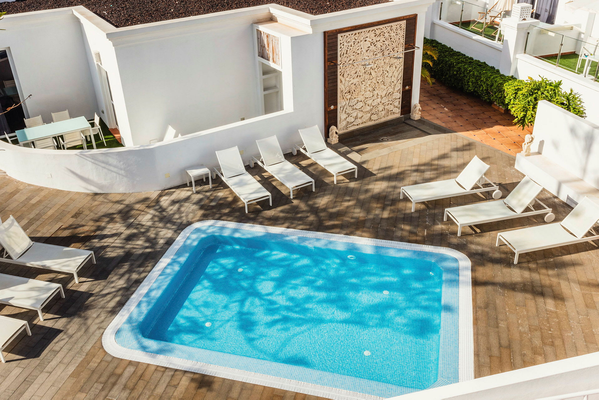En liten swimmingpool med blått vatten omgiven av solstolar och ett trädäck. (AI-genererad text)