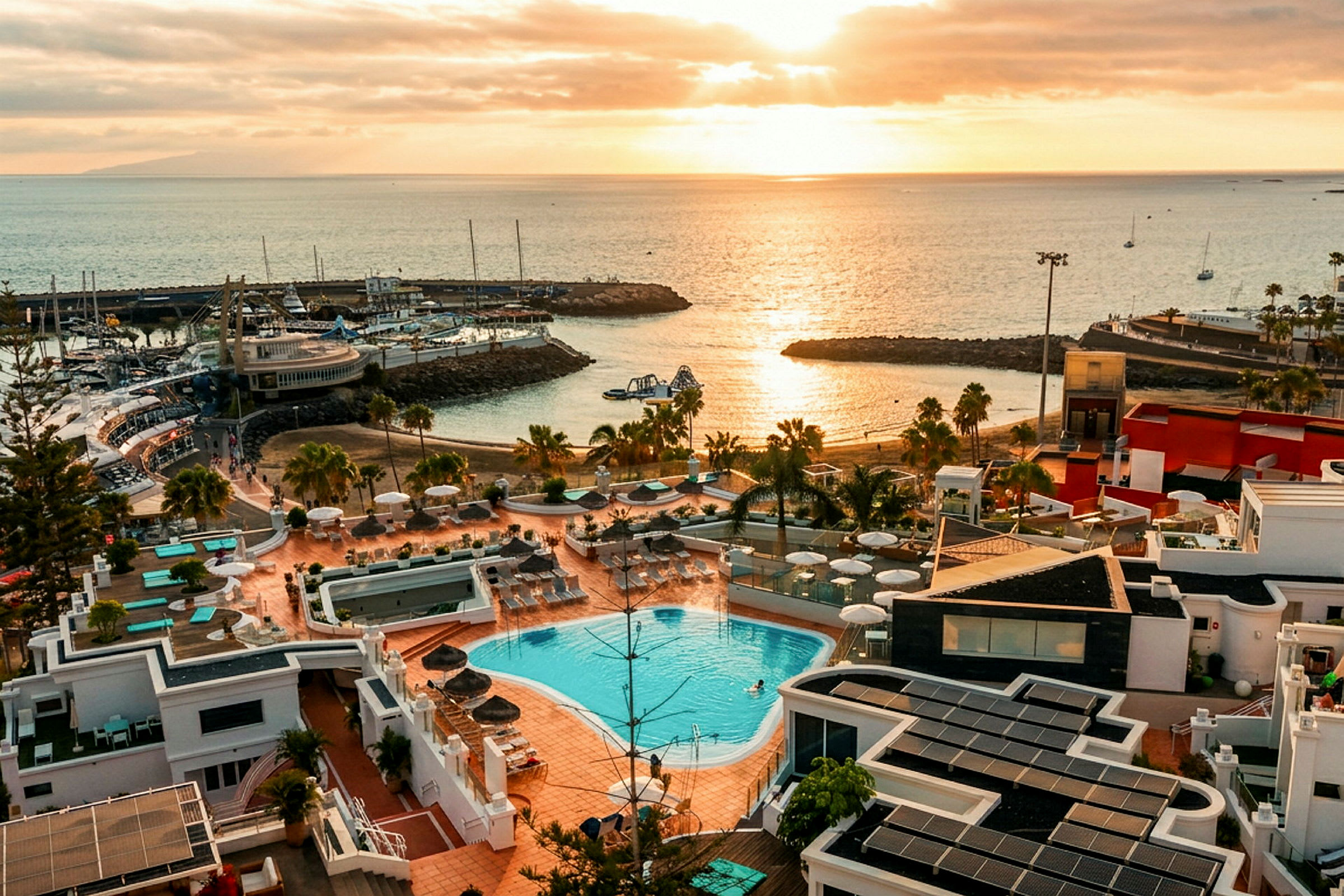 Utsikt över ett kustområde vid solnedgången med en anläggning som har pool och solterrass i förgrunden samt havet och småbåtar i bakgrunden. (AI-genererad text)