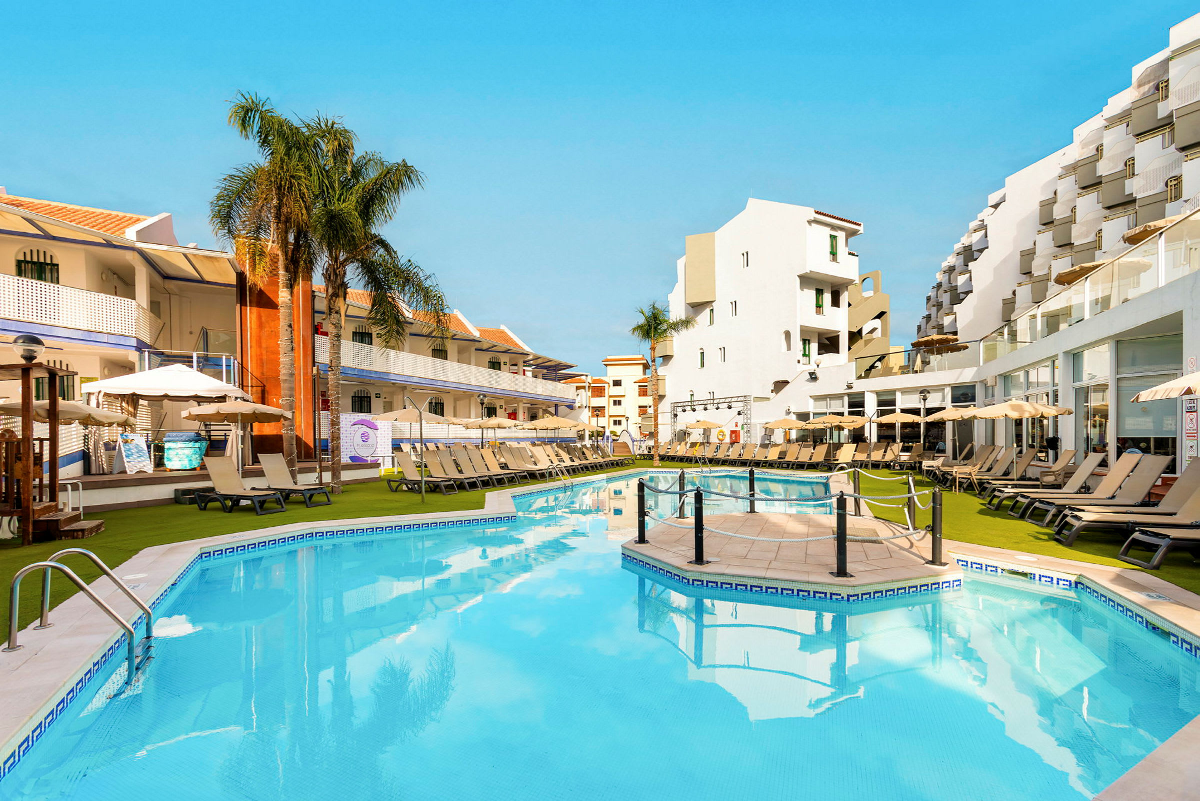Trevliga poolområdet på ett hotell med solstolar, parasoller och omgivande byggnader. (AI-genererad text)