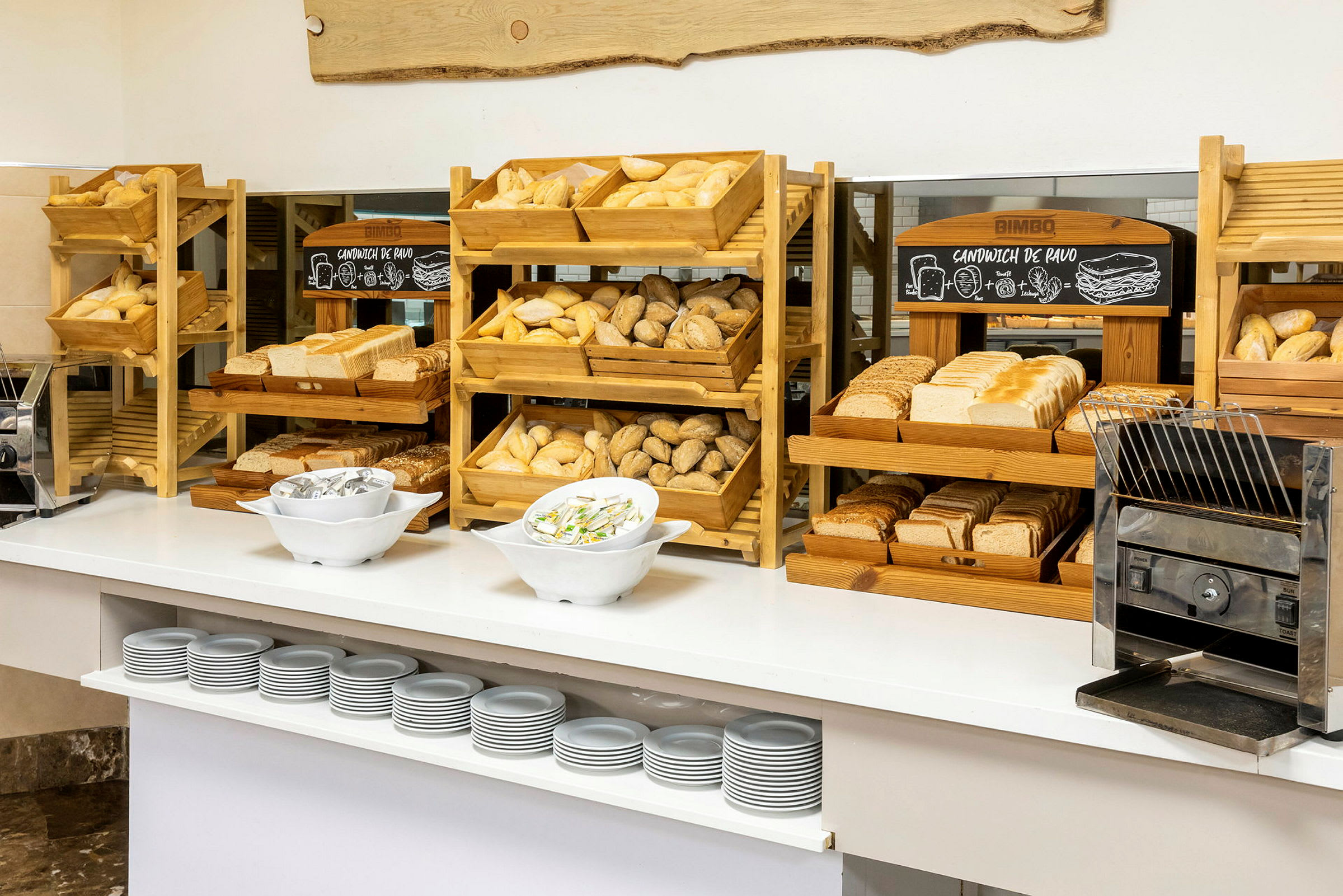 En frukostbuffé med olika sorters bröd, skivade och oskivade, på träställningar och en brödrost. (AI-genererad text)