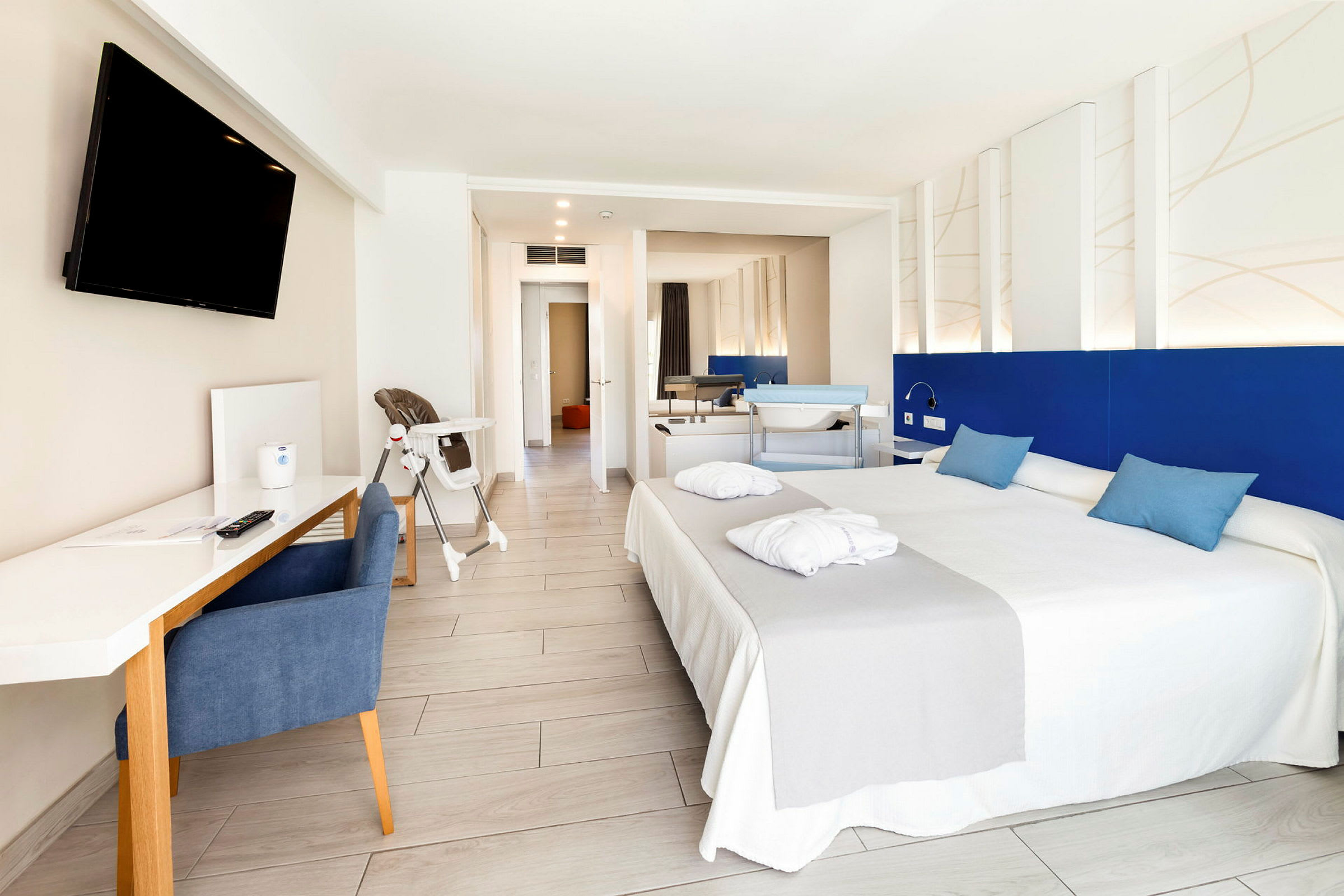 Ett hotellrum med dubbelsäng, skrivbord, TV och babystol. (AI-genererad text)