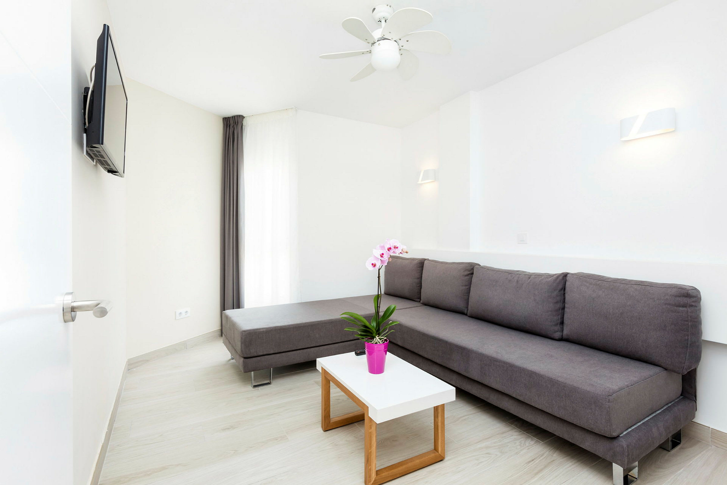 En modern lounge med en grå soffa, vita väggar, och en liten bord med en rosa blomkruka. (AI-genererad text)