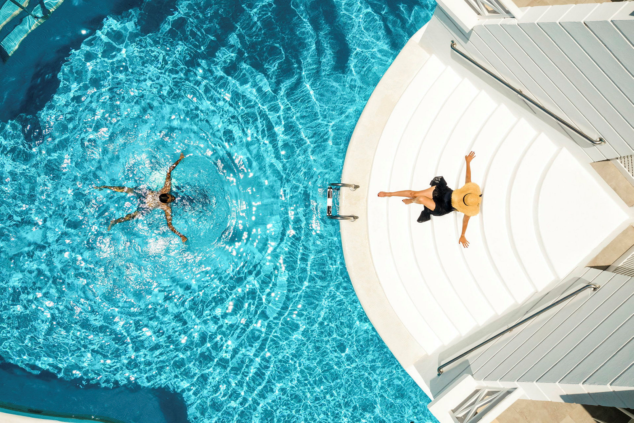 En person simmar i en pool och en annan sitter på trappan vid poolkanten. (AI-genererad text)