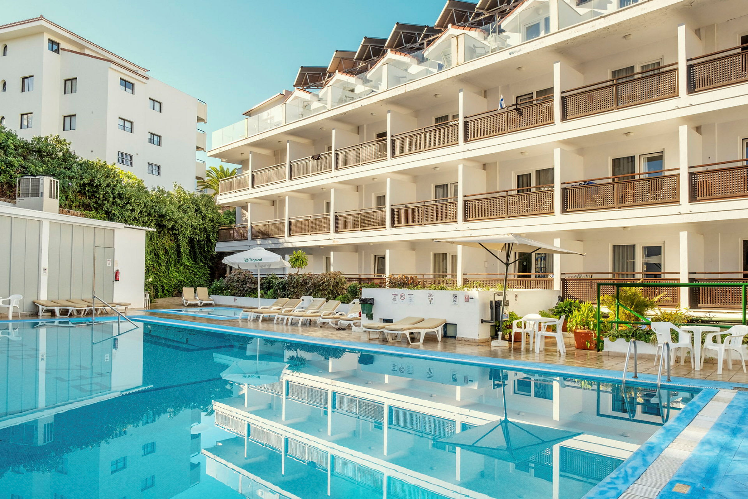 En hotellbyggnad med flera våningar, vid sidan av en utomhuspool och solstolar. (AI-genererad text)
